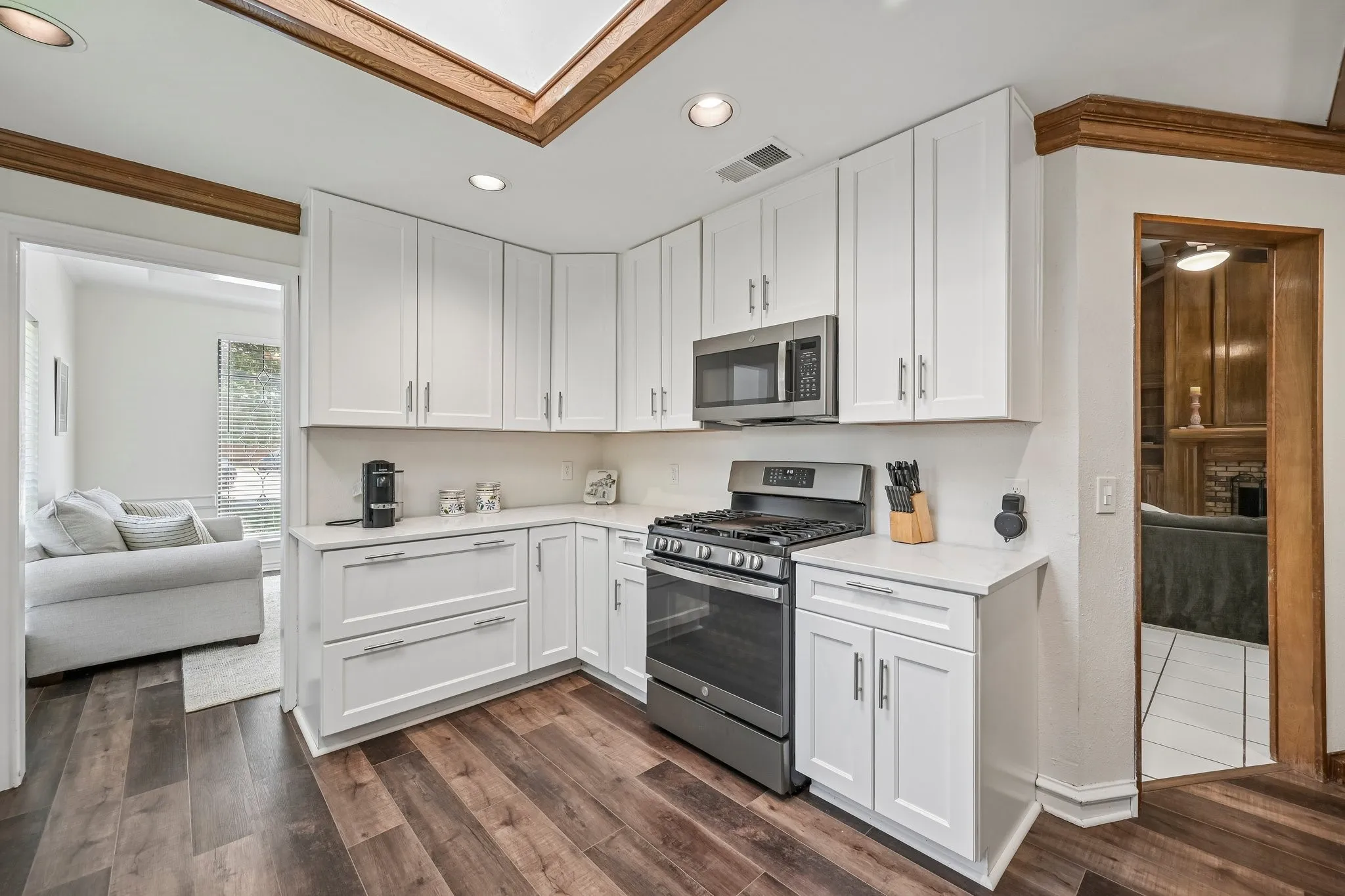 Modern kitchen featuring white shaker-style cabinetry, stainless steel dual-oven range, wood-finish flooring, recessed and skylight ceiling illumination, and a peninsula counter layout with seating capability