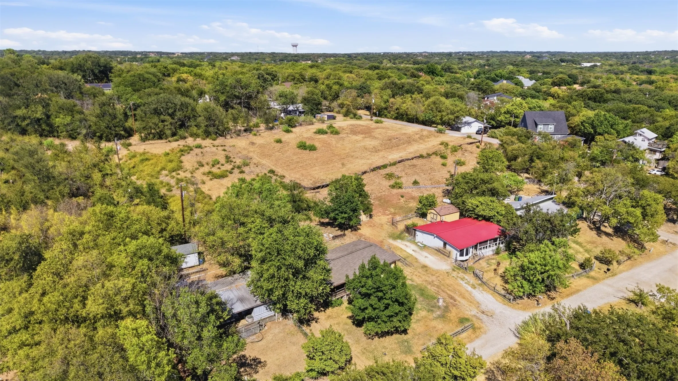 Expansive treed lot featuring multiple structures, including a residence with a vibrant red roof