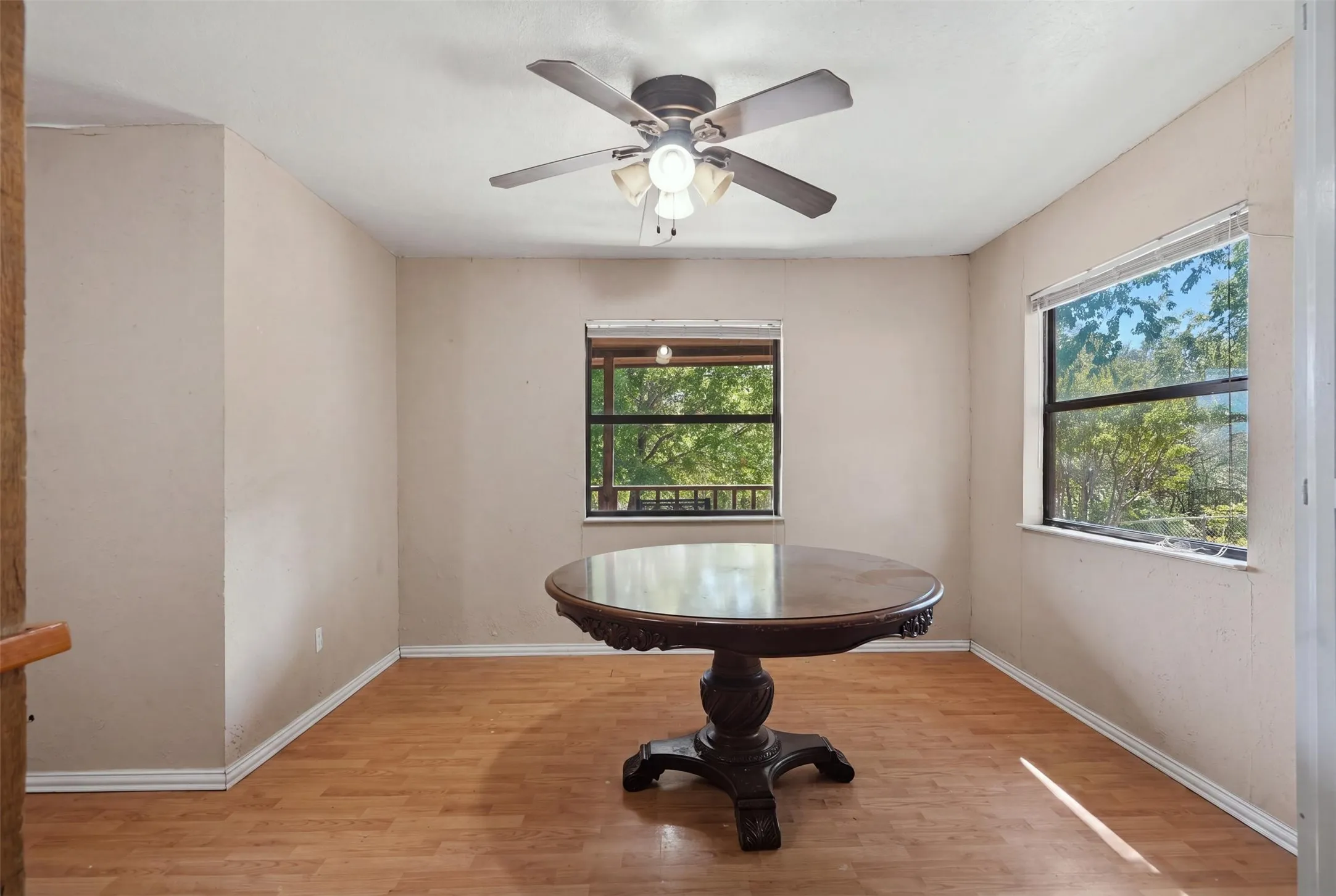 Wood-finish flooring, two large windows, ceiling fan with integrated lighting, and neutral wall tones