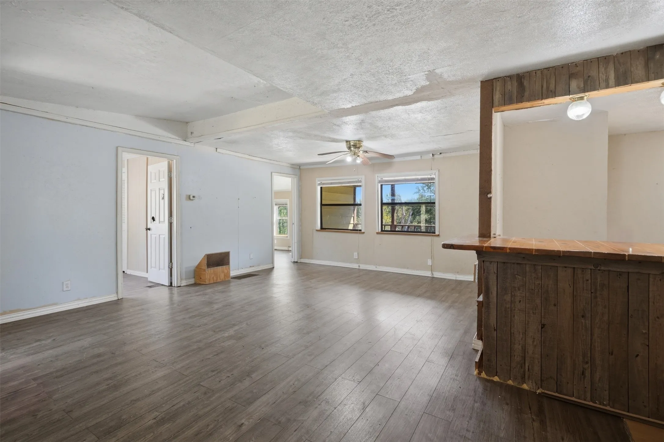 Wood-finish flooring, built-in bar with tiled countertop, ceiling fan, and multiple windows
