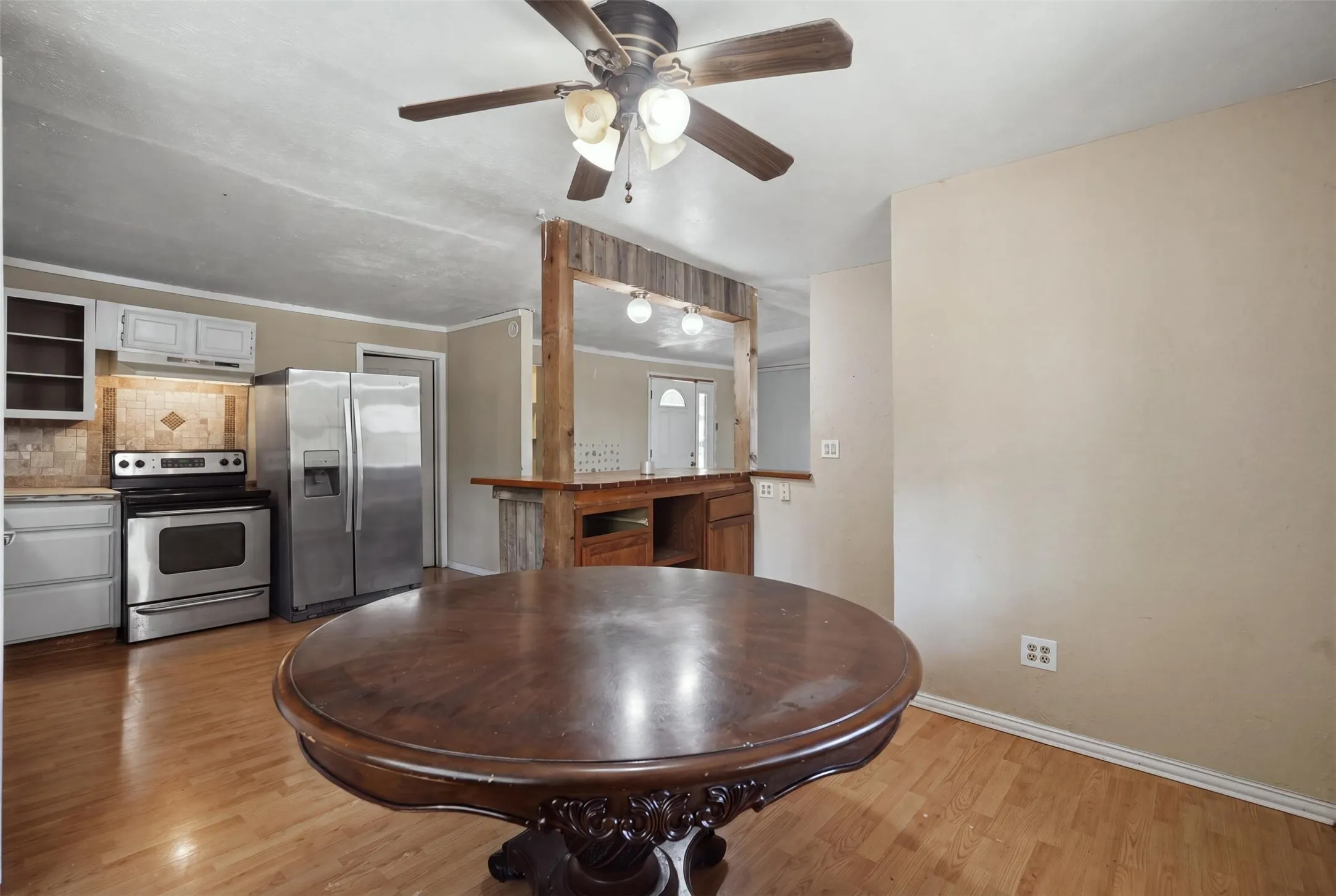Wood-finish flooring throughout, stainless steel appliances, tile backsplash, built-in breakfast bar, and ceiling fan