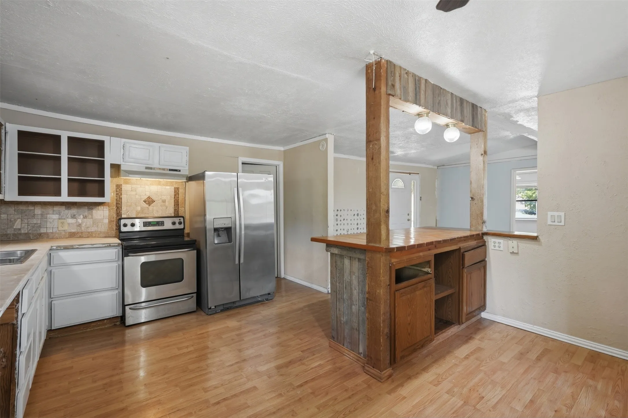 Kitchen featuring wood-finish flooring, white cabinetry, stainless steel appliances, a tiled backsplash, and a wood-paneled breakfast bar
