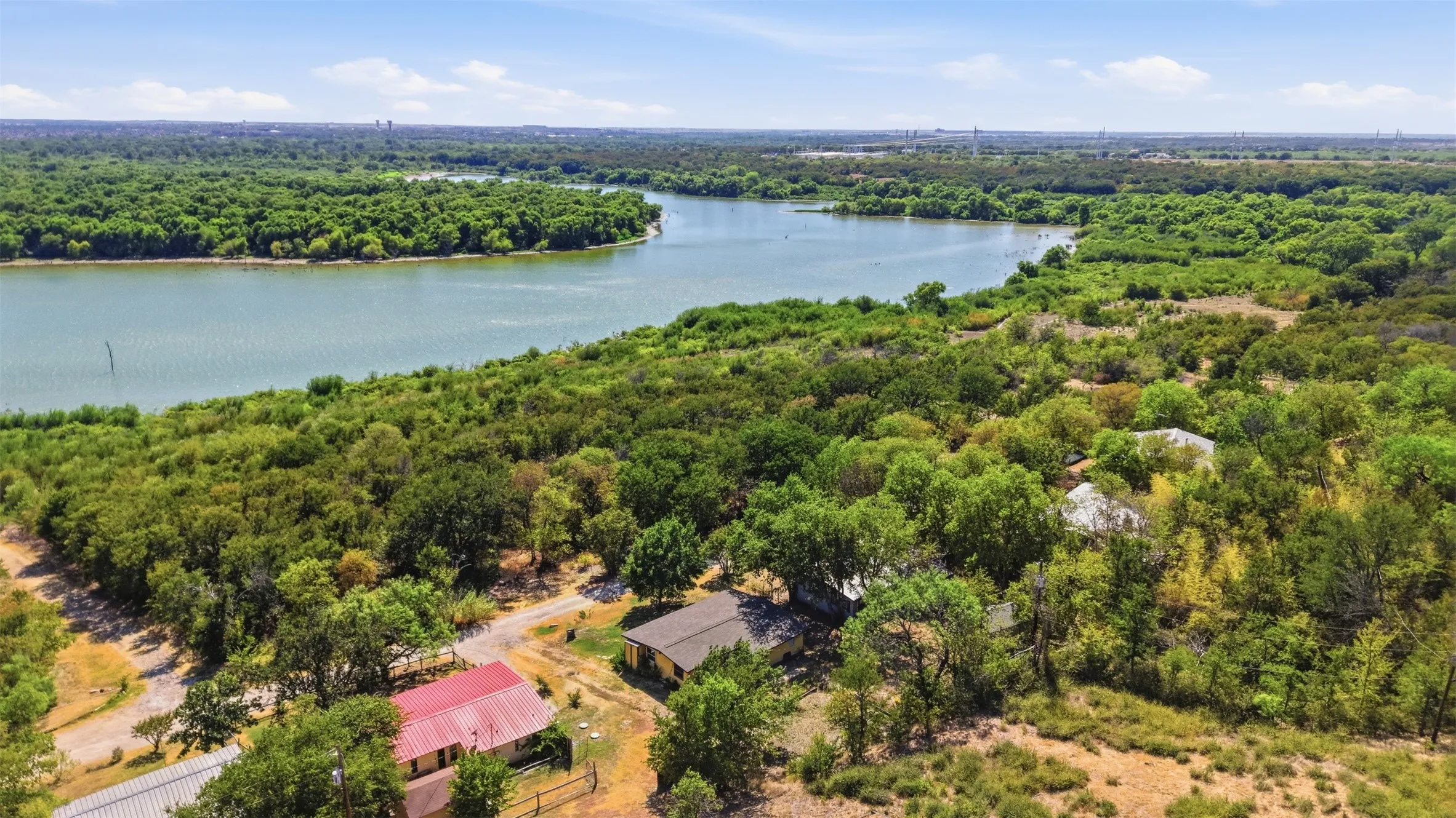 Expansive natural landscape featuring a body of water, dense tree coverage, and multiple residential structures