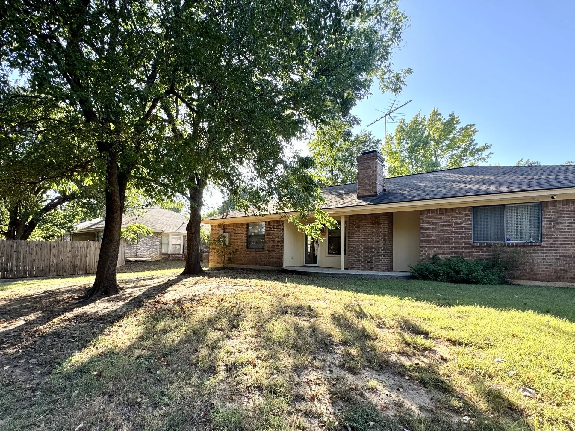 Backyard: brick exterior, dark shingle roof, chimney, concrete patio, mature trees