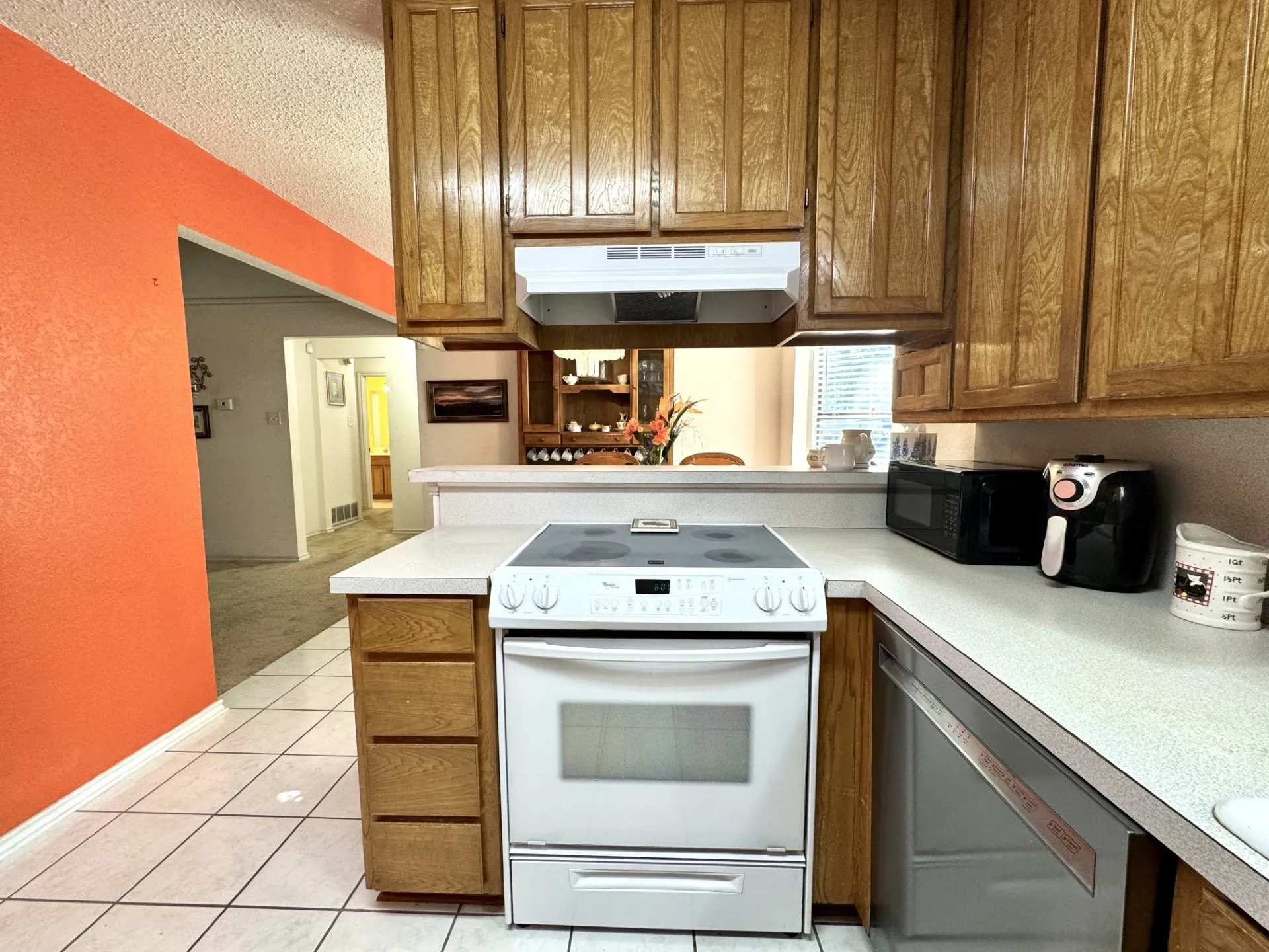 Kitchen: electric range, wood cabinetry, white countertops, stainless steel dishwasher, and white tile flooring.