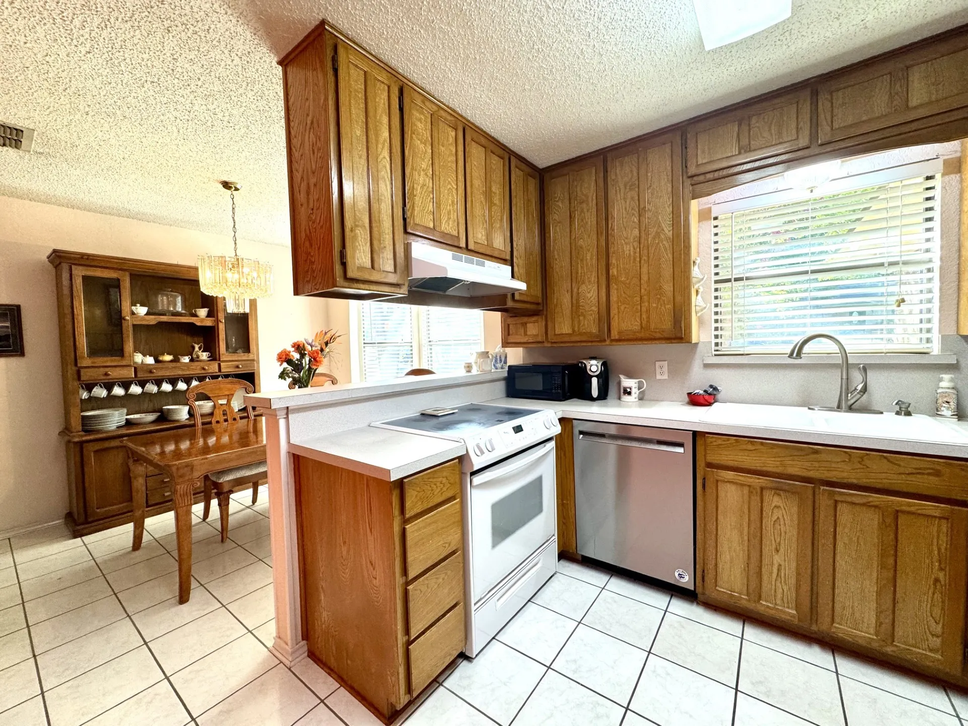 Kitchen Breakfast Bar is great for serving! Double sink, wood cabinetry, SS dishwasher, microwave, electric range with vented hood, and white ceramic tile flooring.