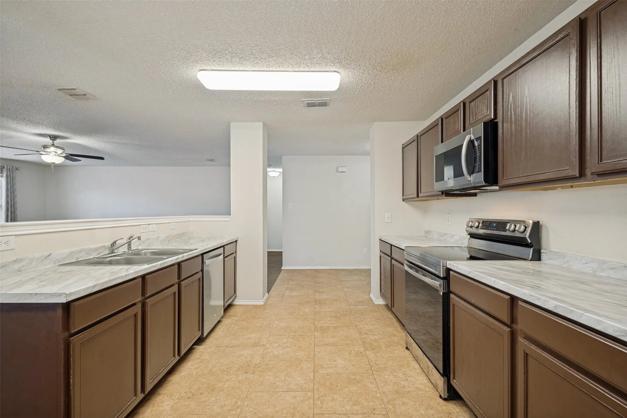 Galley-style kitchen featuring dual sink stations with marble-finish countertops, wood-finish cabinetry, stainless steel appliances, and tile flooring throughout