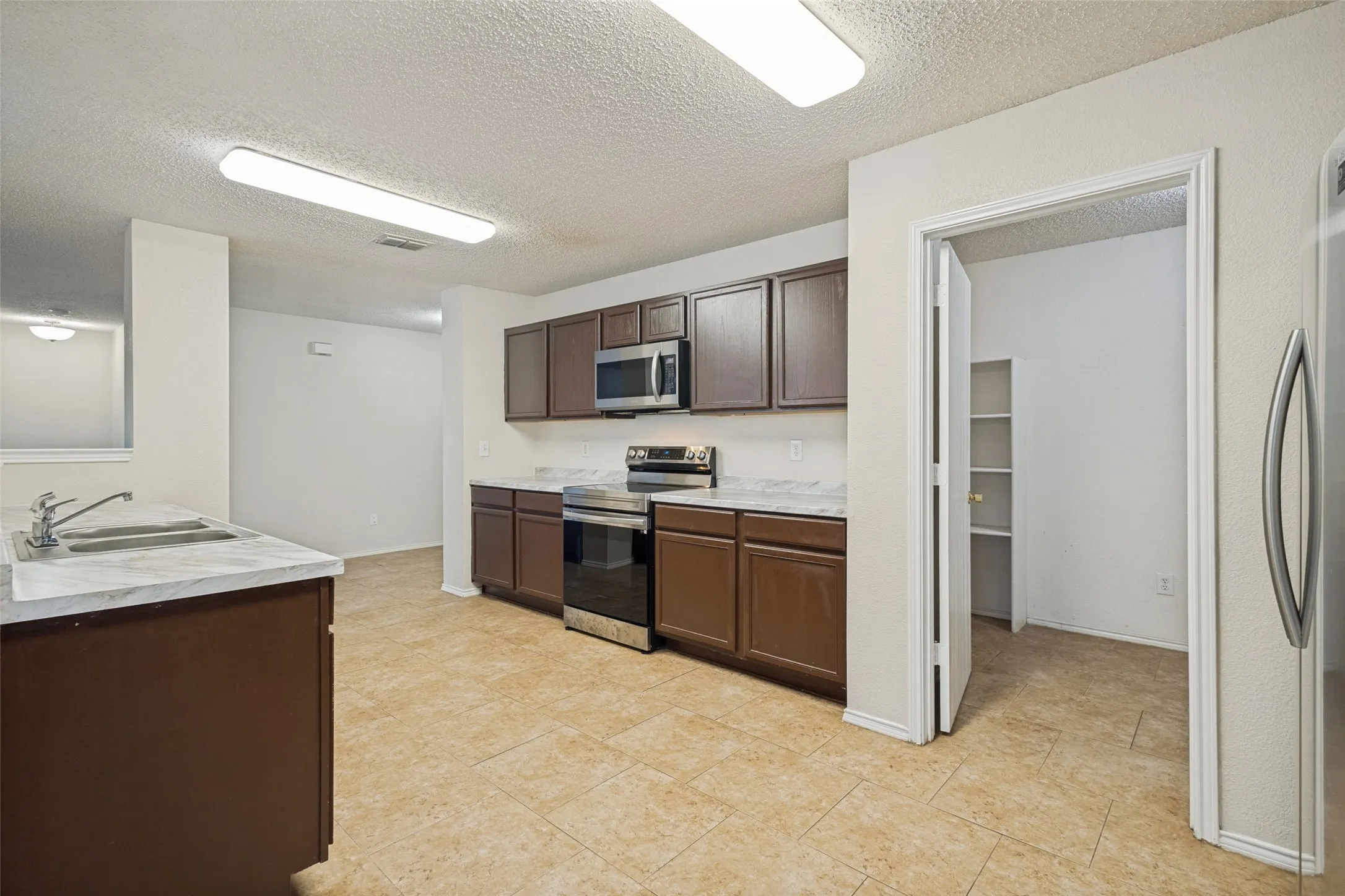 Kitchen featuring dark wood cabinetry, light-toned countertops, stainless steel appliances, a double basin sink, and tile flooring