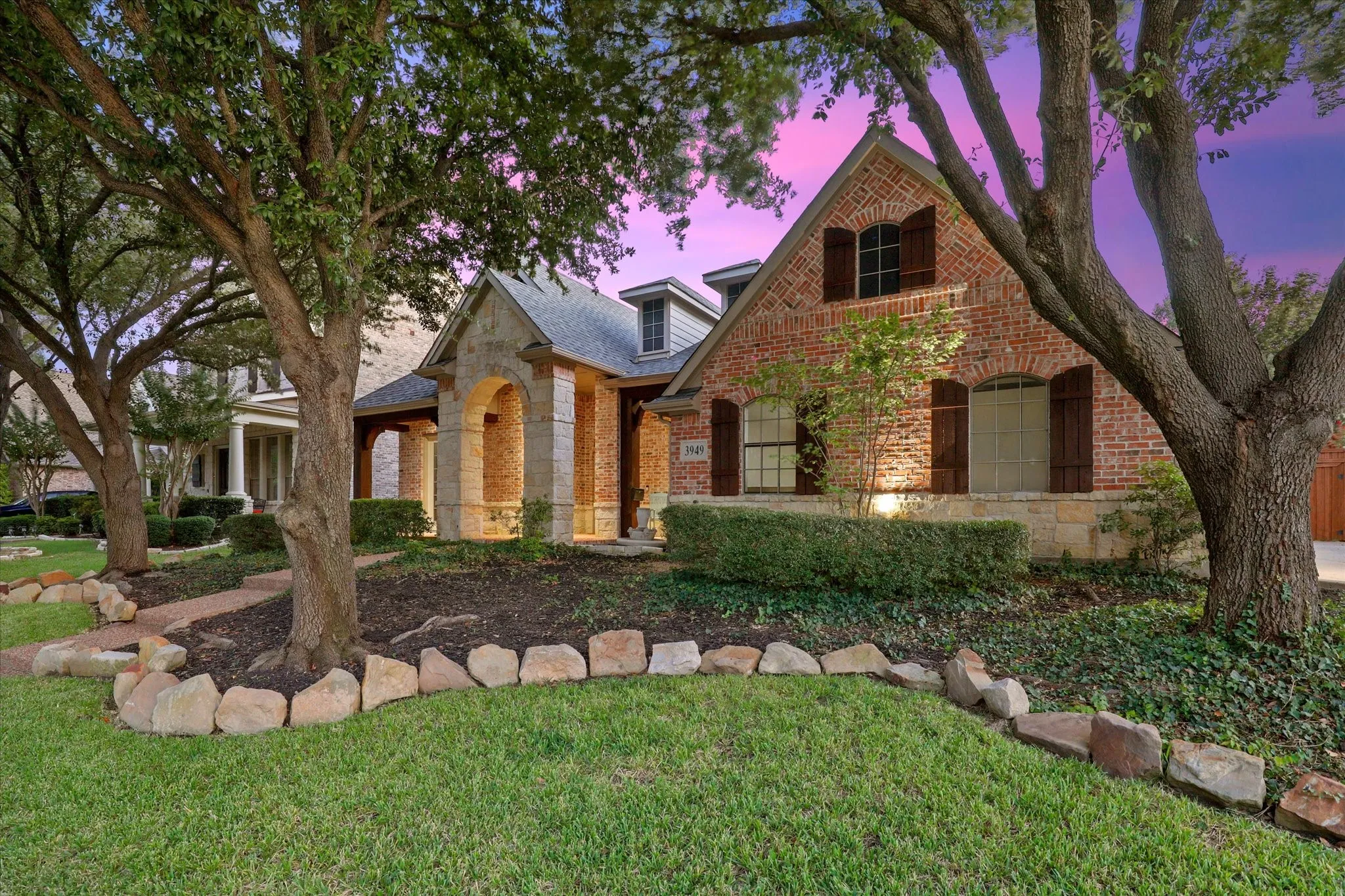 Another view of the front of the home with the brick and rock exterior and beautiful trees.