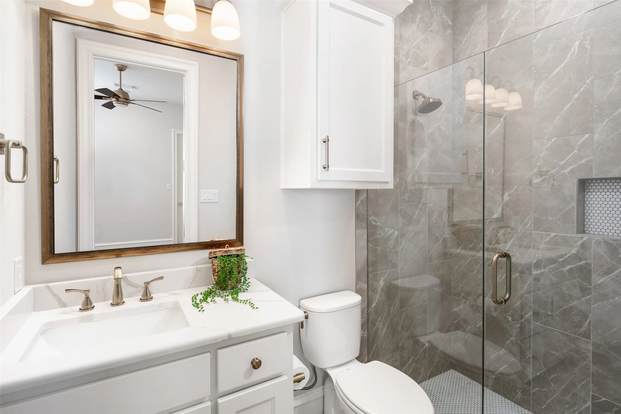 Bathroom featuring a glass-enclosed shower with large format tile, shower niche with mosaic tile, white vanity with integrated sink, and a framed mirror