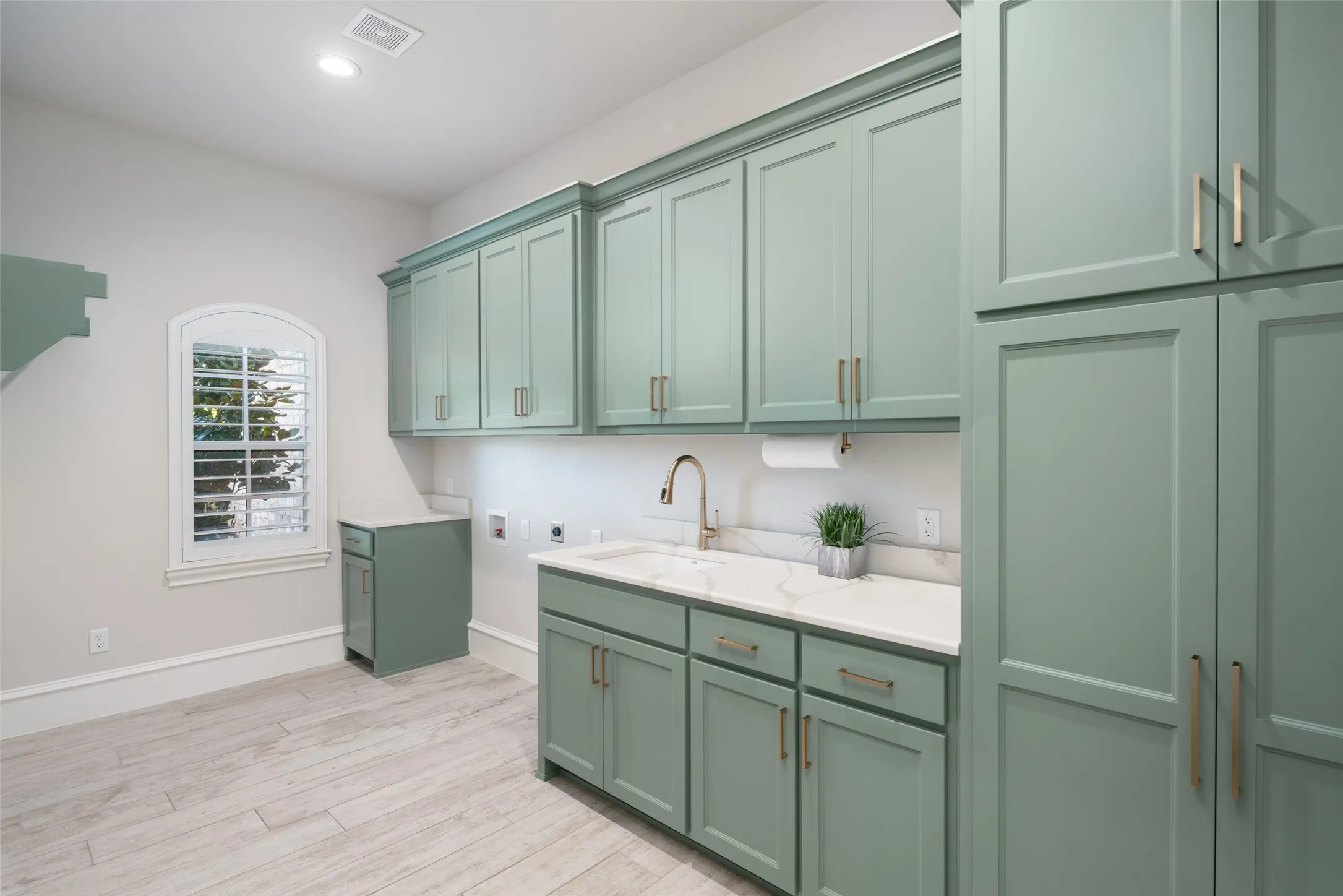 Extensive built-in cabinetry with modern hardware, stone countertops, integrated sink with gooseneck faucet, arched window, and wood-finish flooring