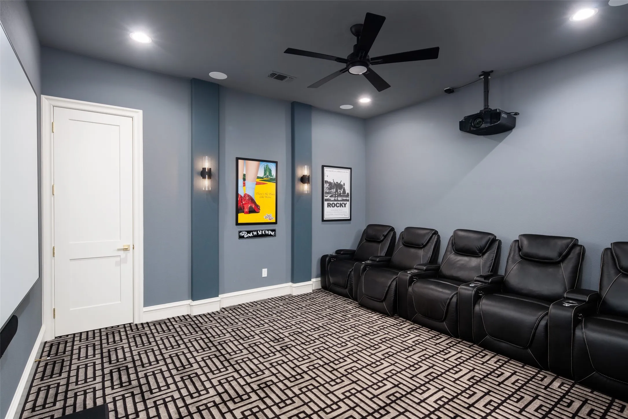 Recessed lighting, wall-mounted sconces, ceiling fan, architectural wall paneling, and a mounted projector