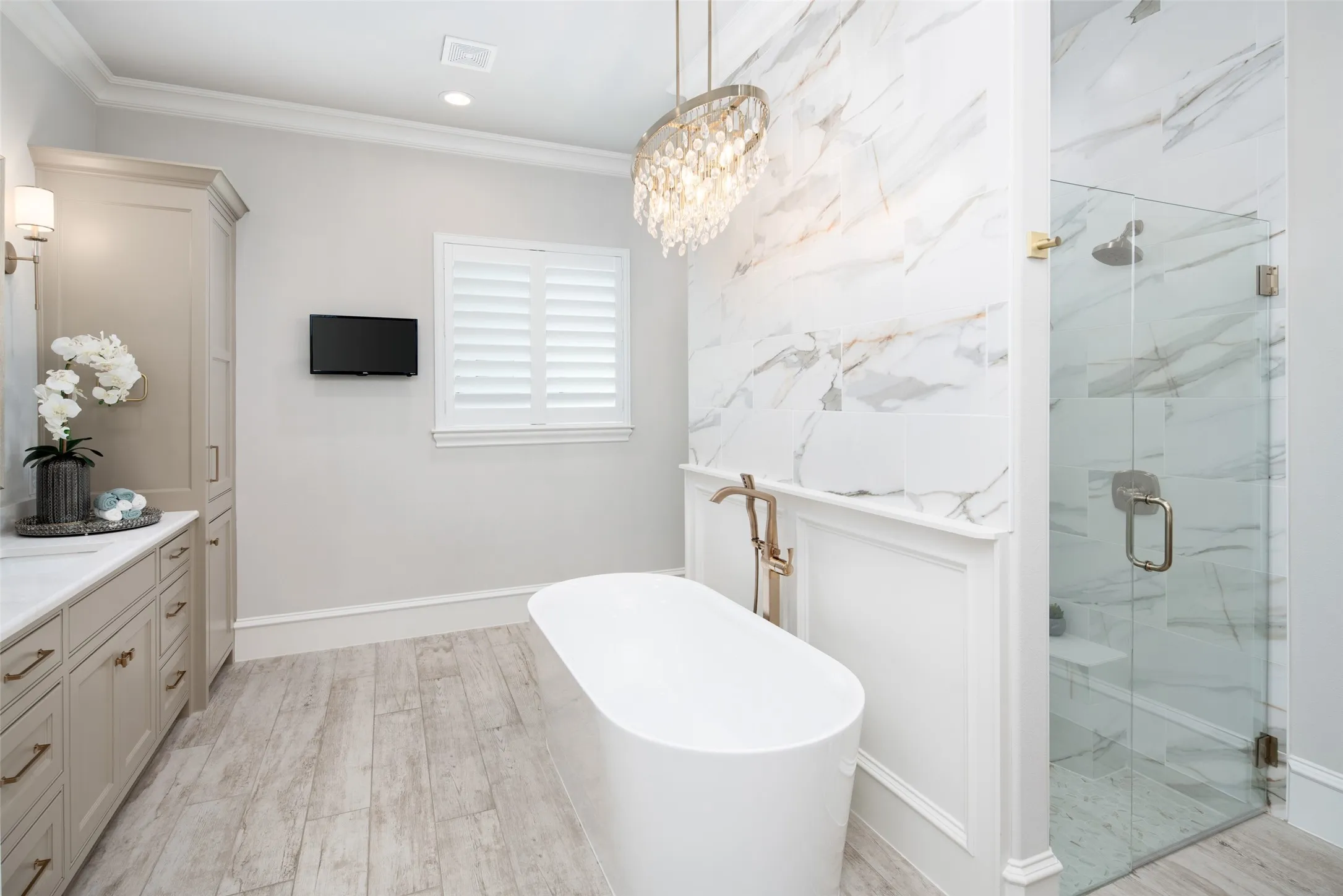 Freestanding soaking tub with floor-mounted faucet, glass-enclosed shower with bench, full-height marble-patterned wall tile, and plank-style flooring