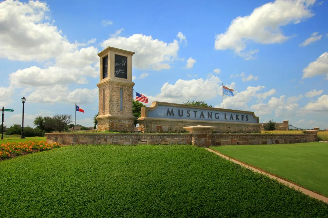 Stone-clad entry monument featuring a clock tower, integrated signage, and lush landscaping