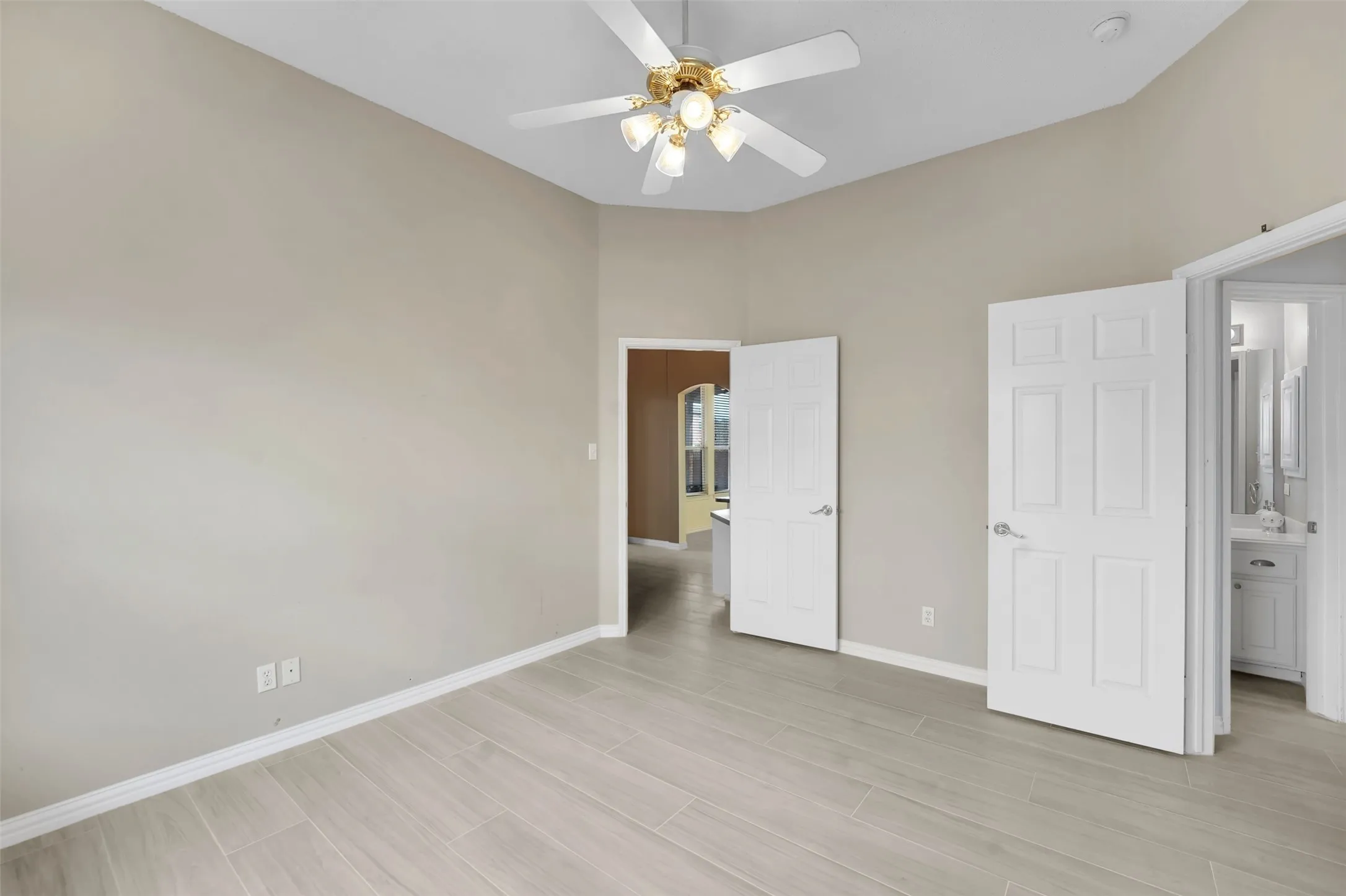 Spacious bedroom featuring light wood-finish flooring, neutral wall finishes, and abundant natural light from recessed ceiling fixtures