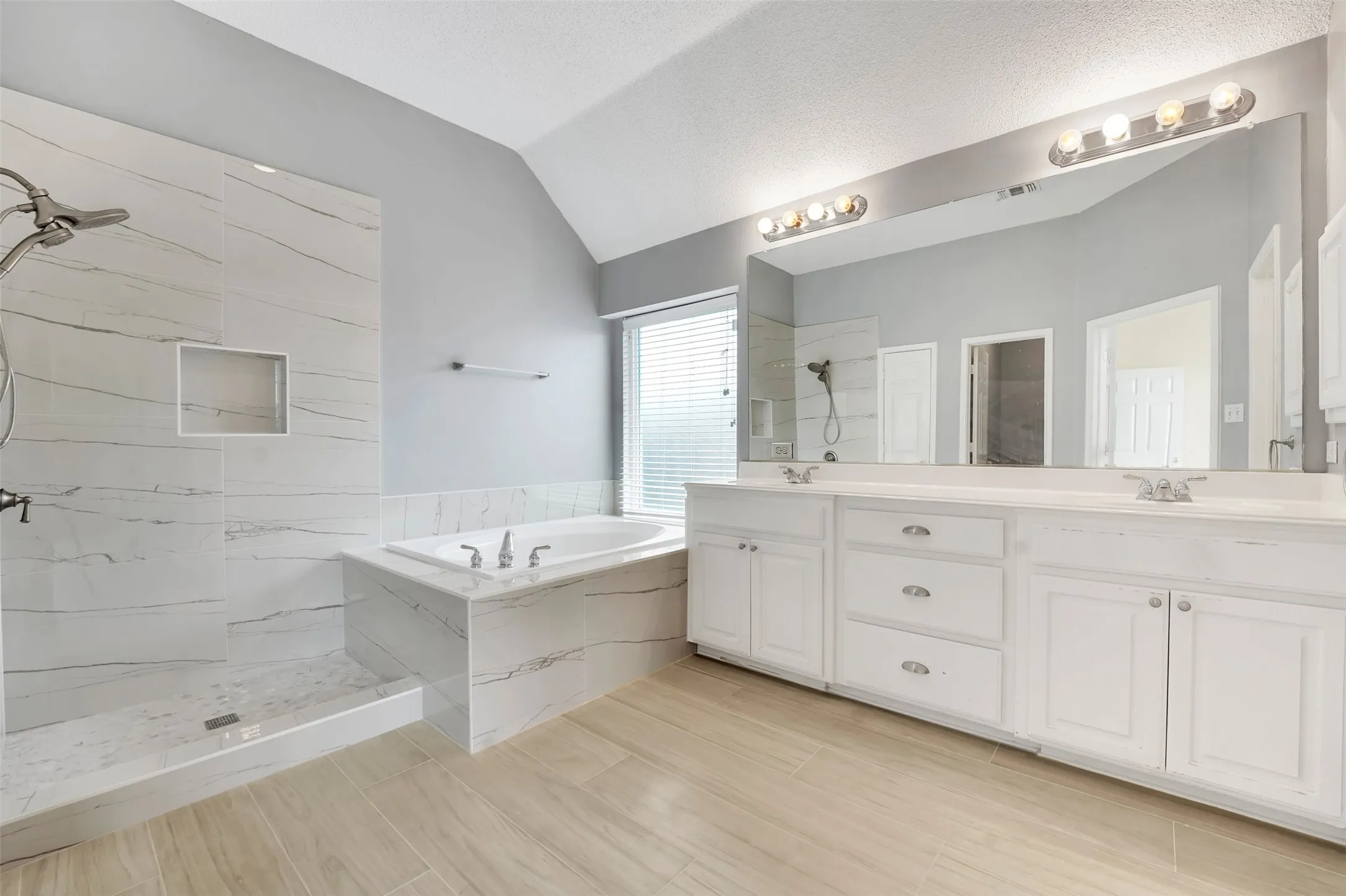 Spa-inspired primary bathroom featuring dual vanities with white cabinetry, brushed nickel hardware, and an expansive mirror wall