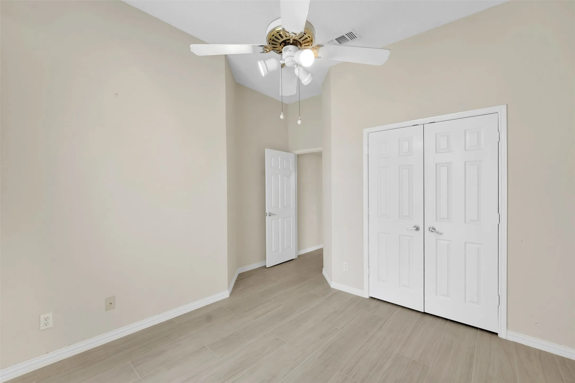 Spacious bedroom featuring wood-finish flooring, ceiling fan with integrated lighting, and dual closet doors with six-panel styling