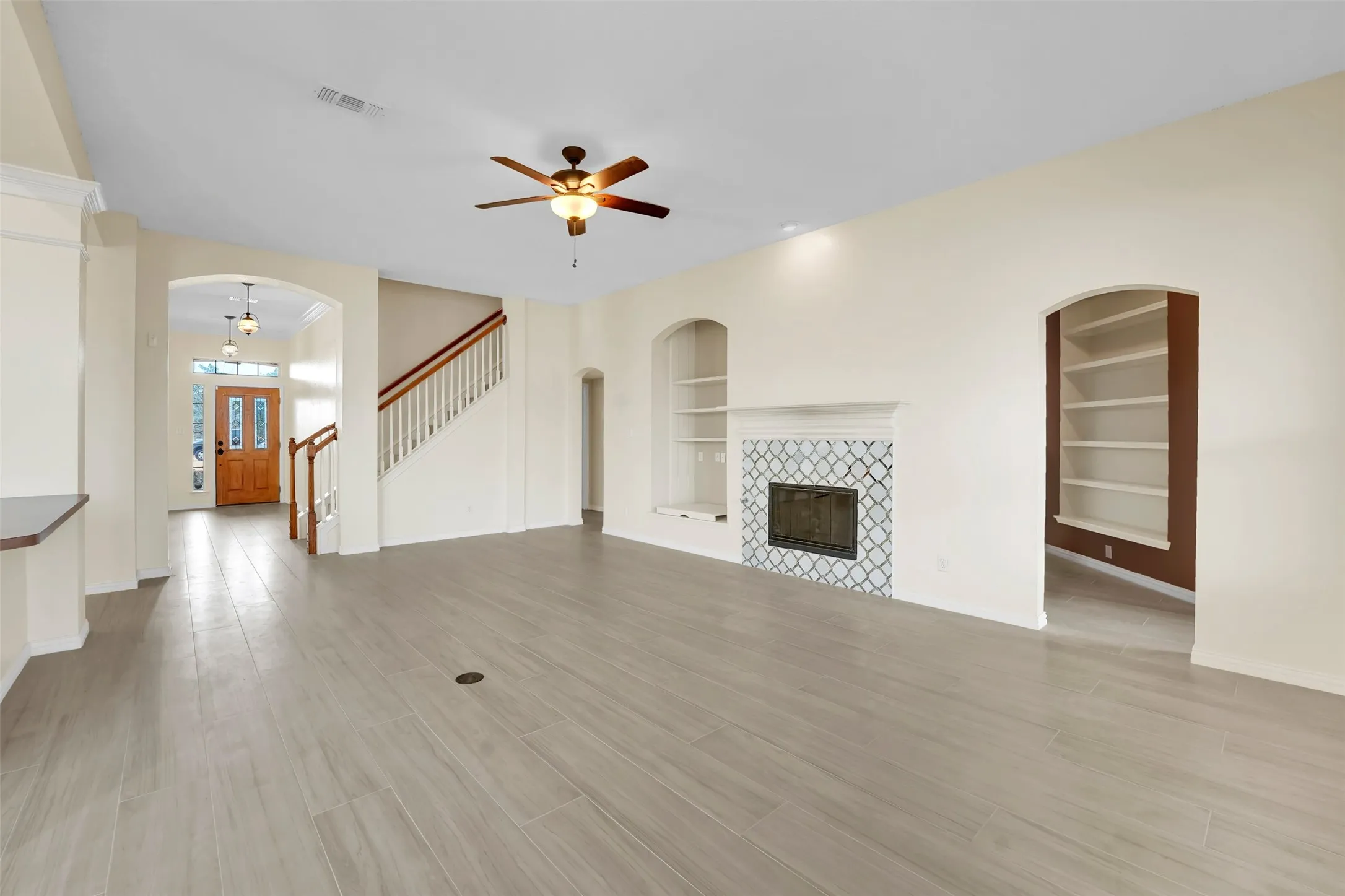 Spacious living area featuring wood-finish flooring, a decorative ceiling fan, and a fireplace with decorative tile surround
