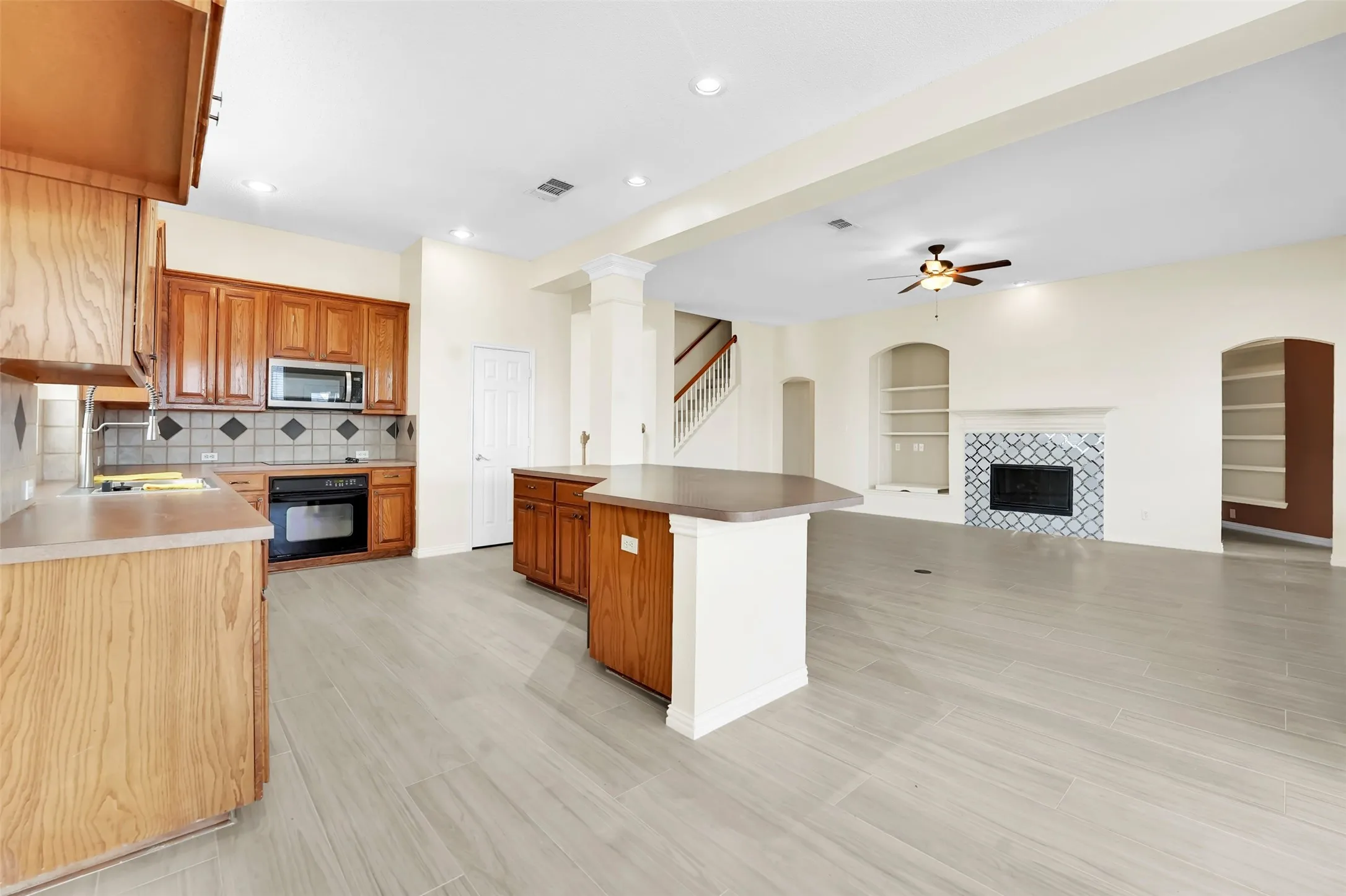 Open-concept living space featuring wood-finish flooring throughout, a wood-finish kitchen with stainless steel appliances and granite countertops, a large center island with contrasting white cabinetry, ceiling fan, and recessed lighting