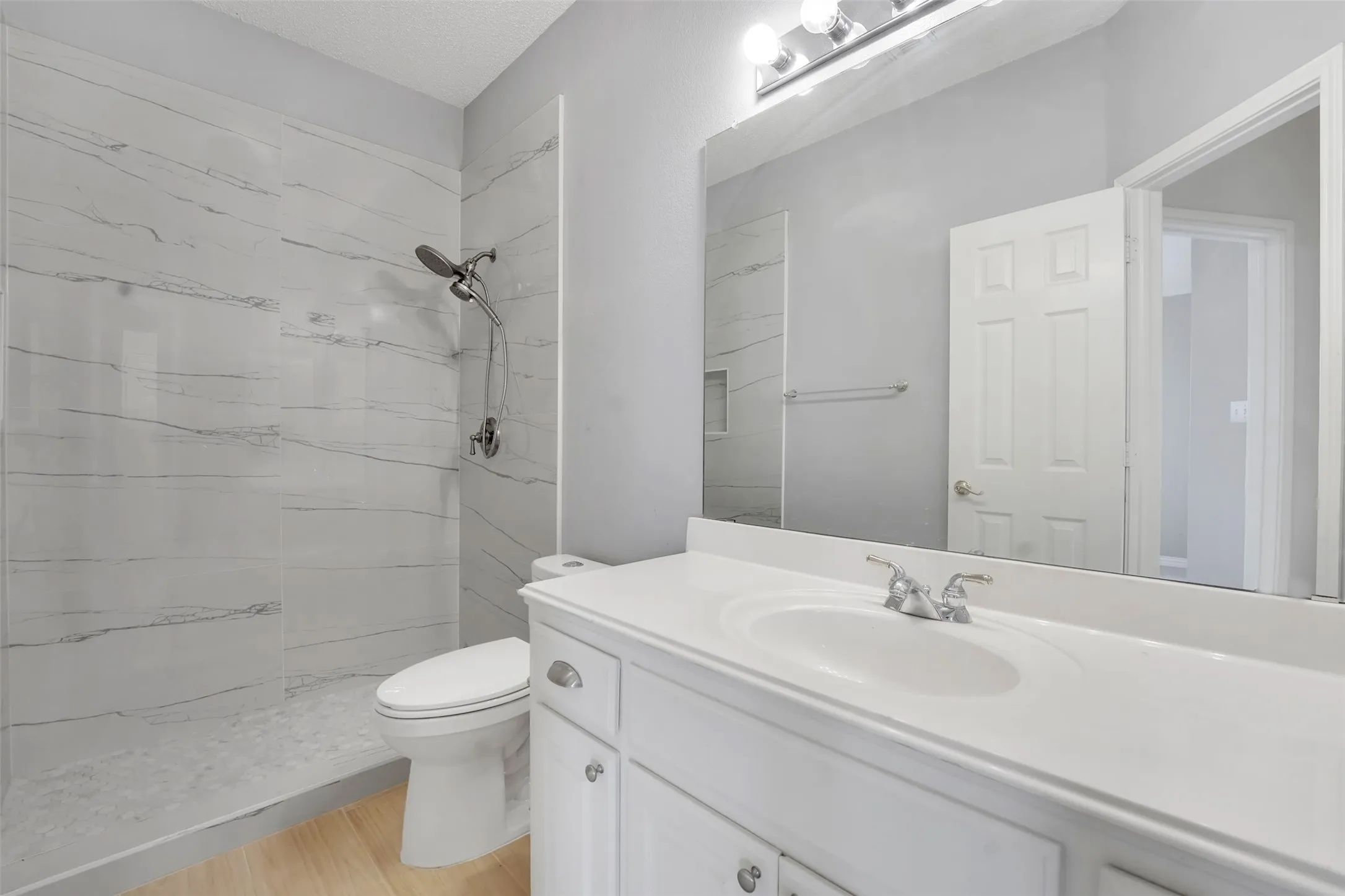 Spa-inspired bathroom featuring a frameless glass shower enclosure with horizontal tile detailing, dual vanity with white cabinetry and rectangular undermount sinks, large mirror with integrated lighting, and white subway tile walls throughout