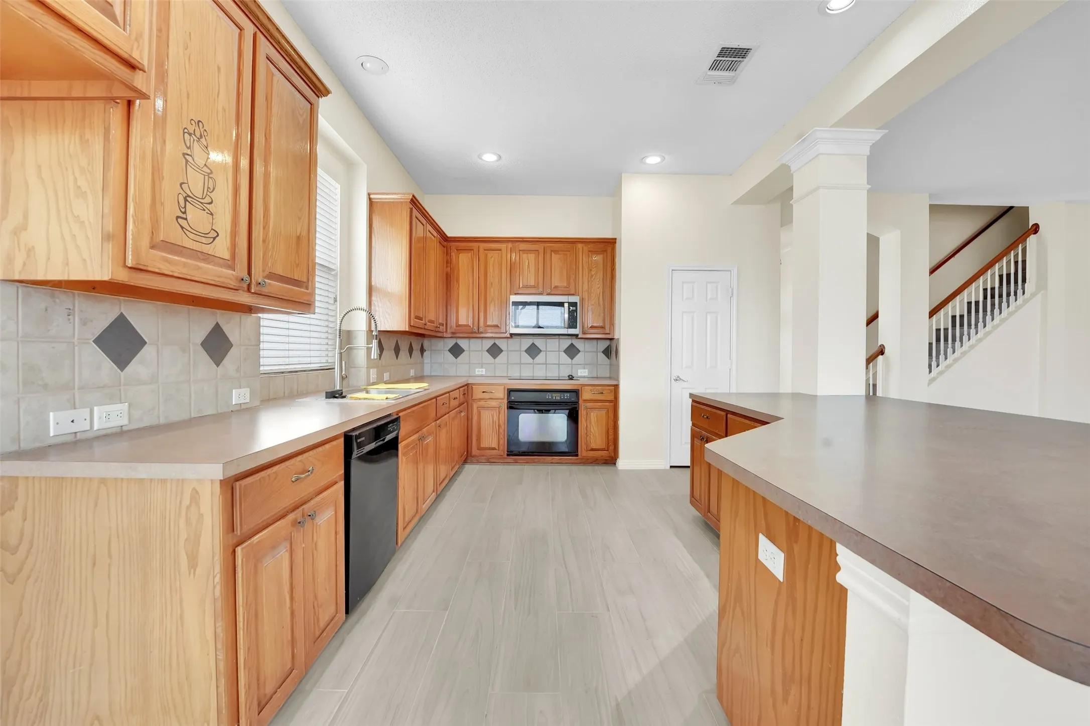 Chef's kitchen showcasing warm wood cabinetry, stainless steel appliances, ceramic tile backsplash with diamond accents, gray wood-finish flooring, and a generous island with contrasting countertop