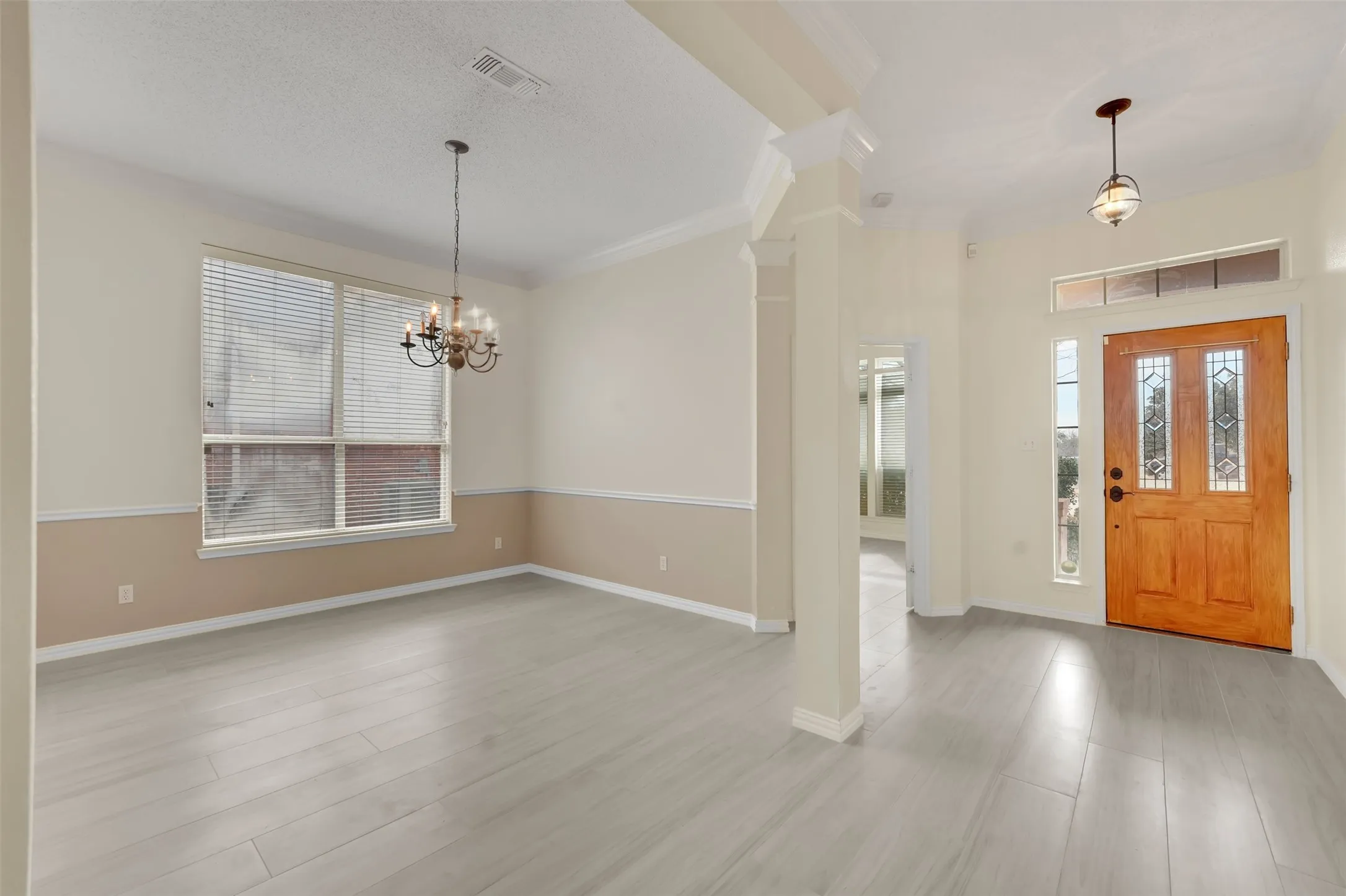 Welcoming foyer and dining area featuring gleaming wood-finish flooring, soaring ceilings with architectural columns, and abundant natural light from multi-pane windows