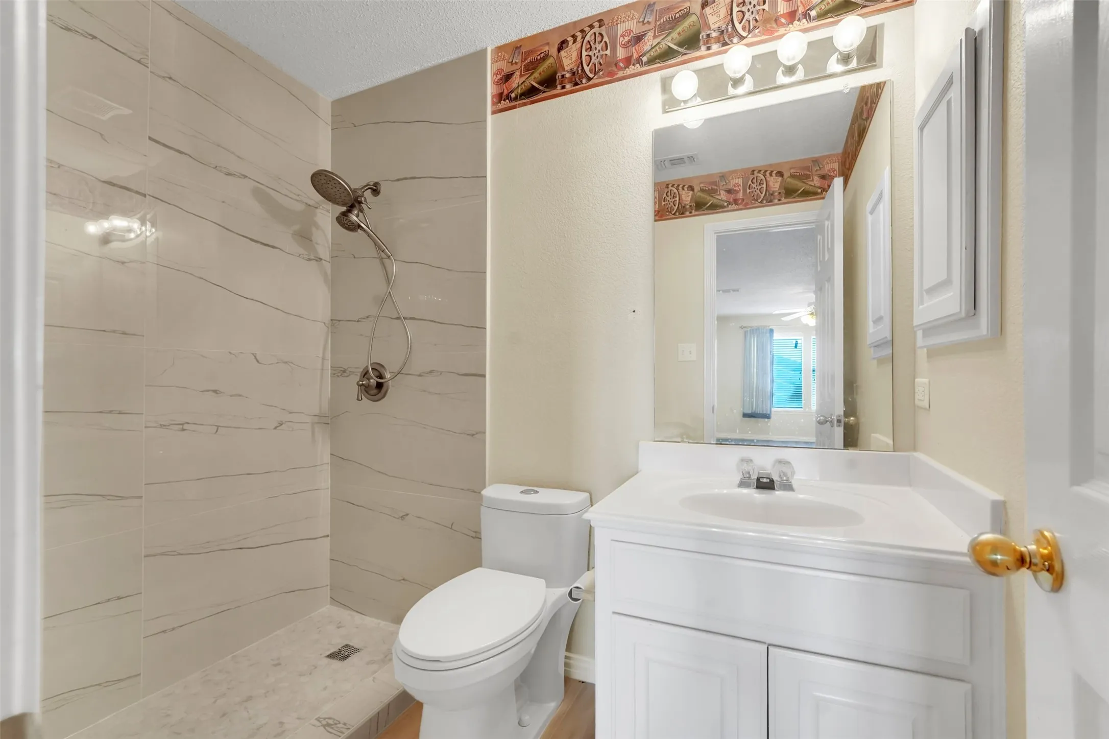 Walk-in shower with large-format tile surround, white vanity with integrated sink, and wall-mounted vanity mirror