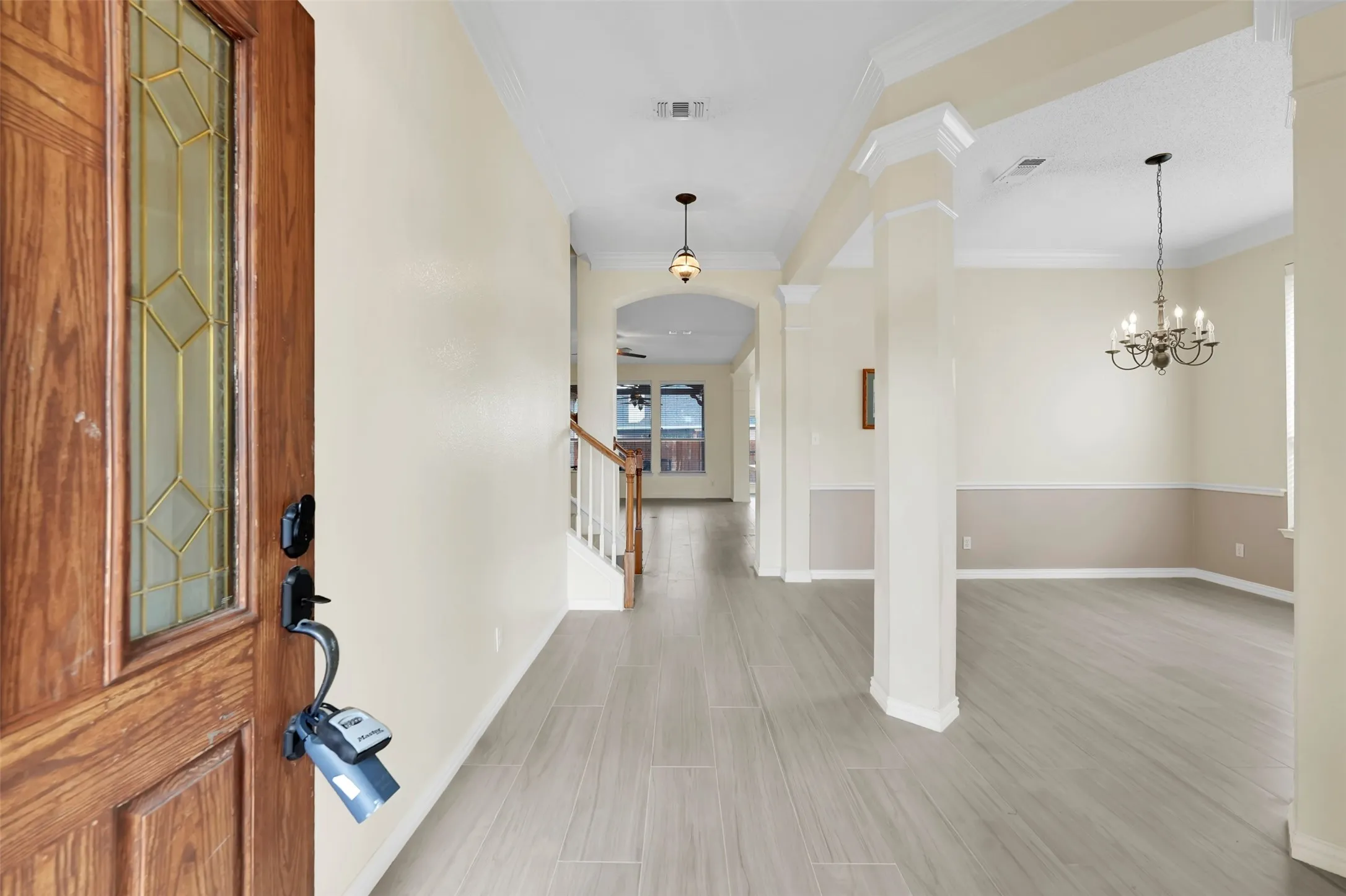 Elegant foyer and hallway featuring wood-finish flooring throughout, white painted walls with neutral upper trim, and classic architectural columns