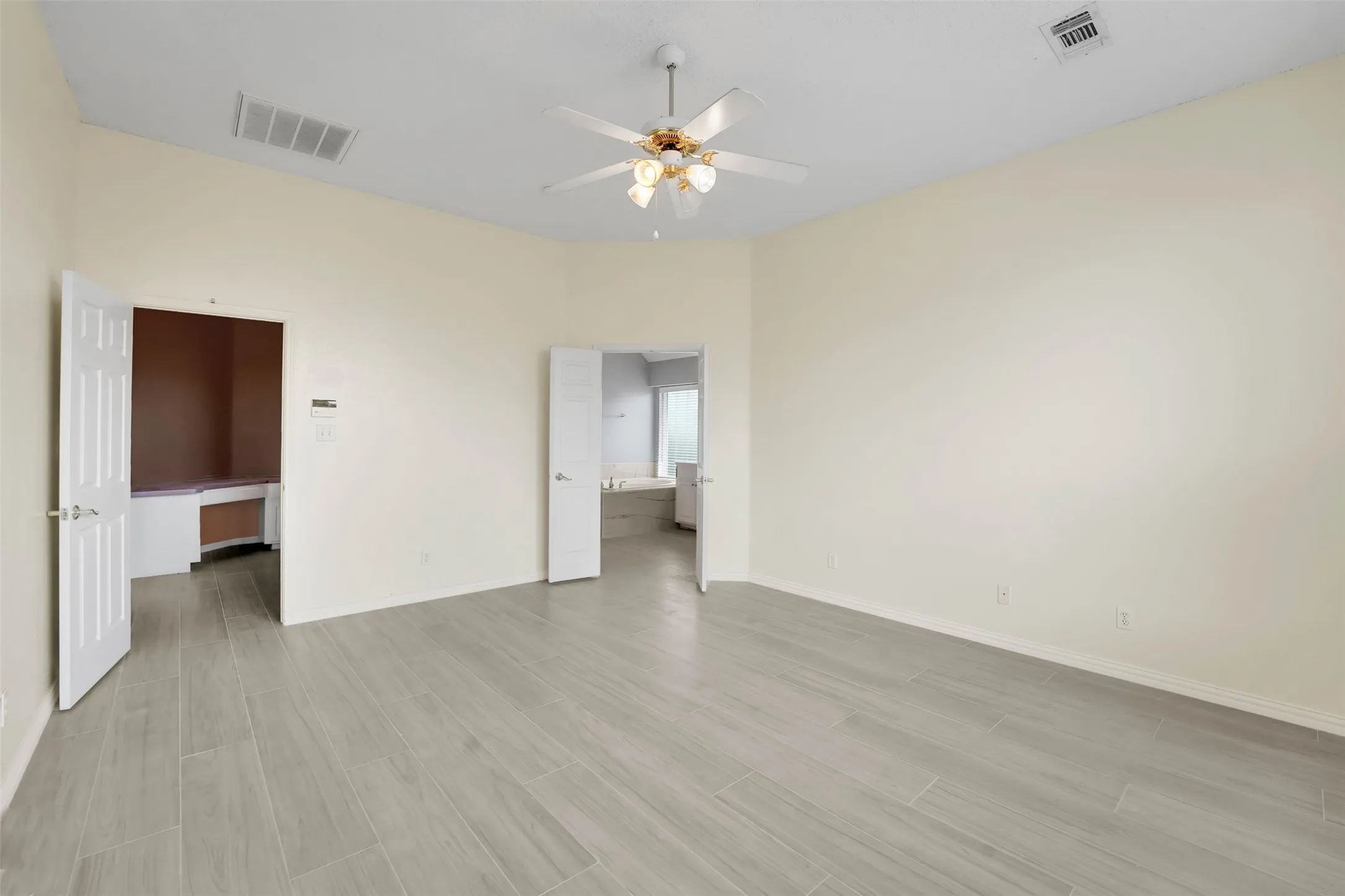 Spacious primary living area featuring wood-finish flooring throughout, ceiling fan with integrated lighting, and multiple doorways providing access to adjoining rooms