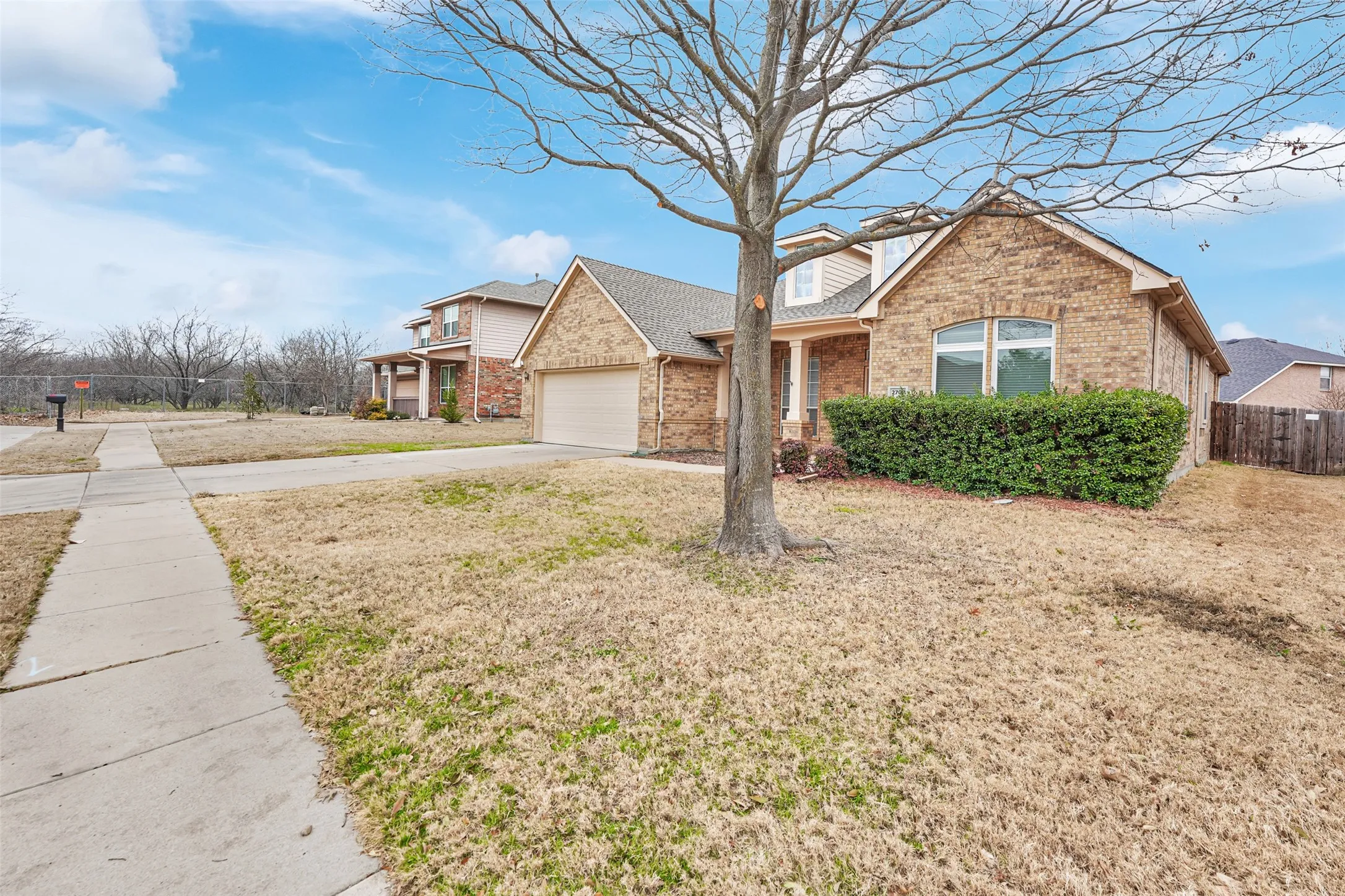 Charming brick residence featuring a manicured front lawn, mature shade tree, and concrete driveway
