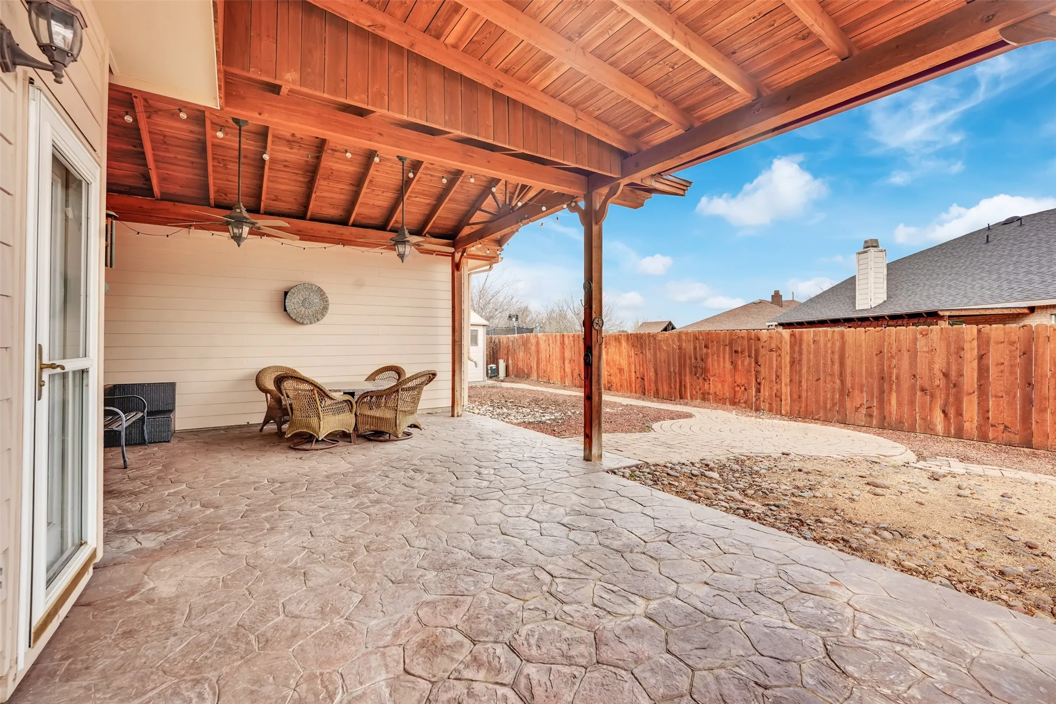 Expansive stamped concrete patio with attached wood-beam pergola overhead, offering generous outdoor entertaining space