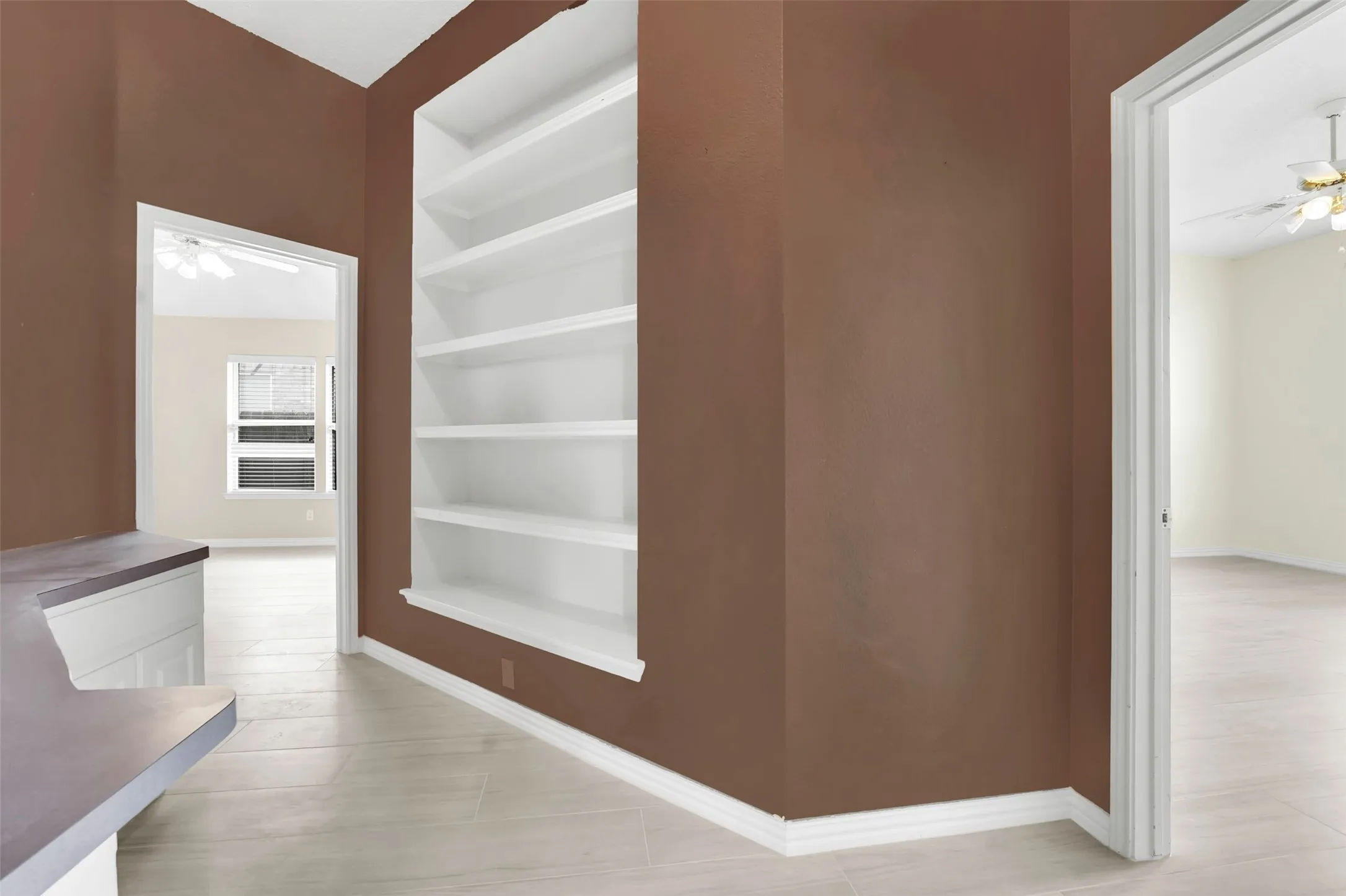 Modern hallway showcasing warm taupe walls, light wood-finish flooring, and custom white built-in shelving