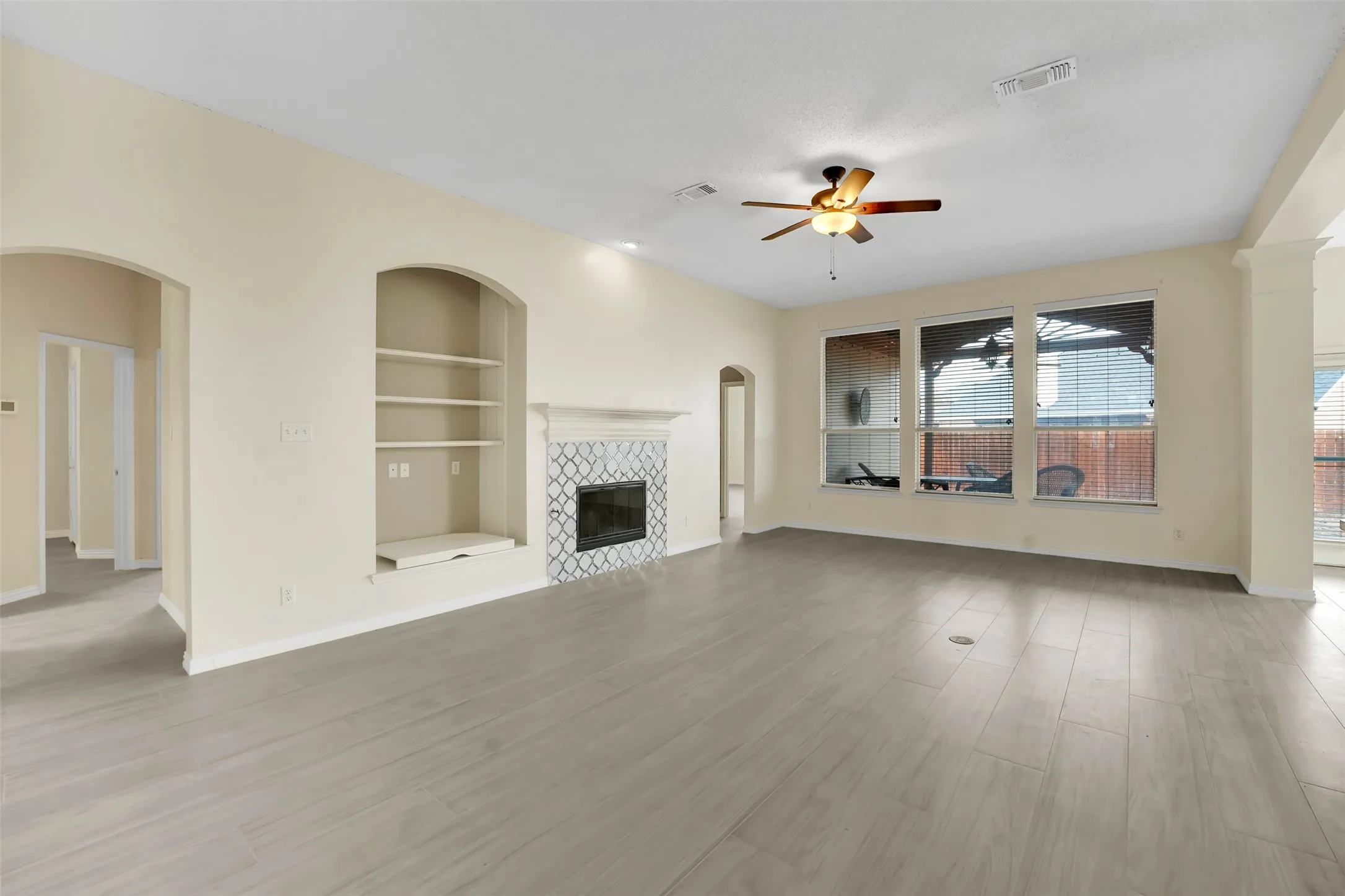 Spacious living room showcasing gleaming wood-finish flooring, recessed ceiling lighting, and a ceiling fan