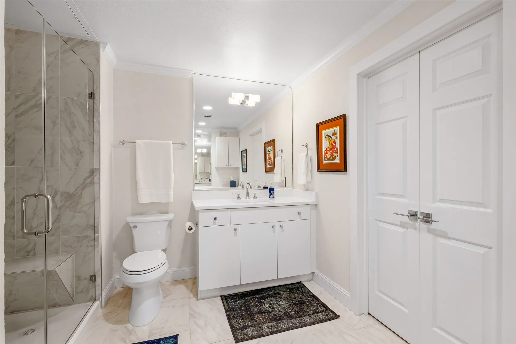 Glass-enclosed shower with a built-in bench, marble-finish tile, and a single vanity with storage