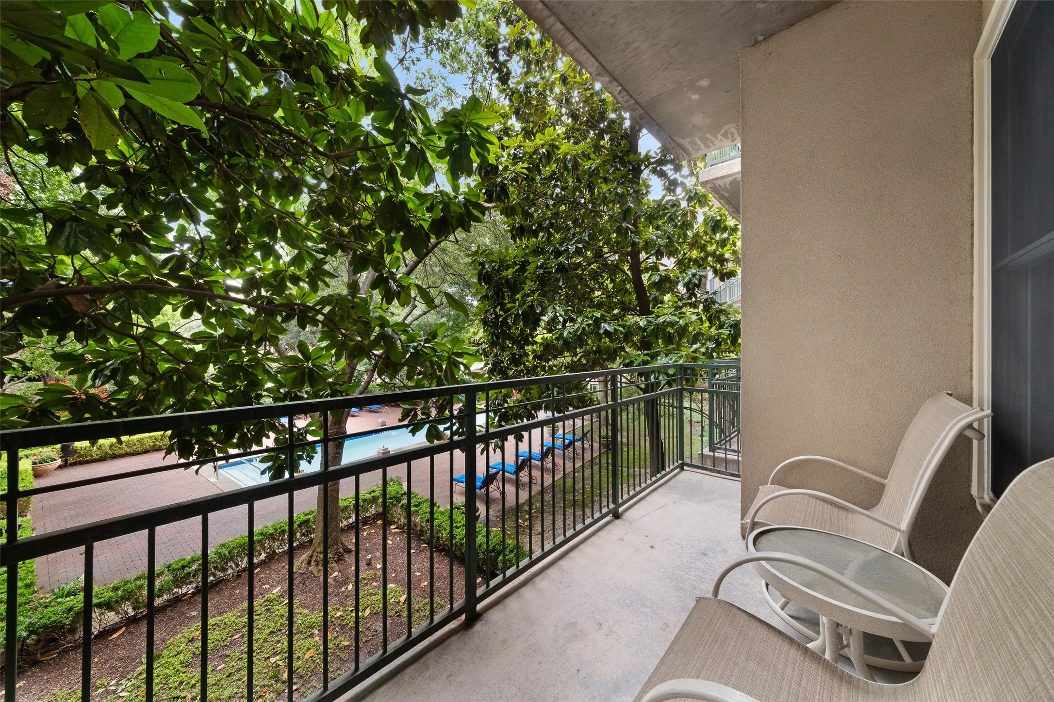 Balcony with dark metal railings, concrete flooring, and surrounding mature trees