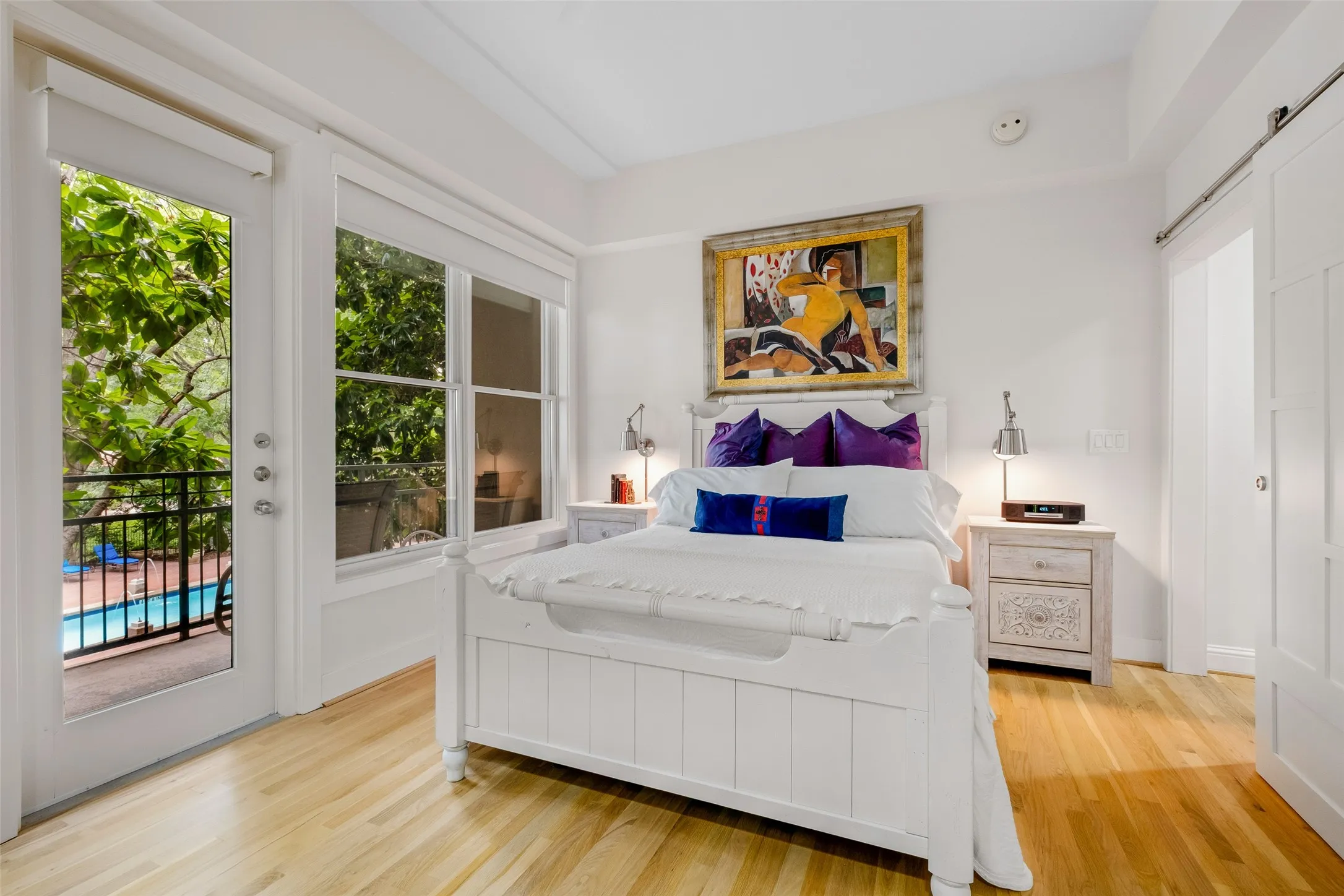 Hardwood flooring throughout, white framed door leading to a balcony with black railing, white framed windows, and a white sliding barn door