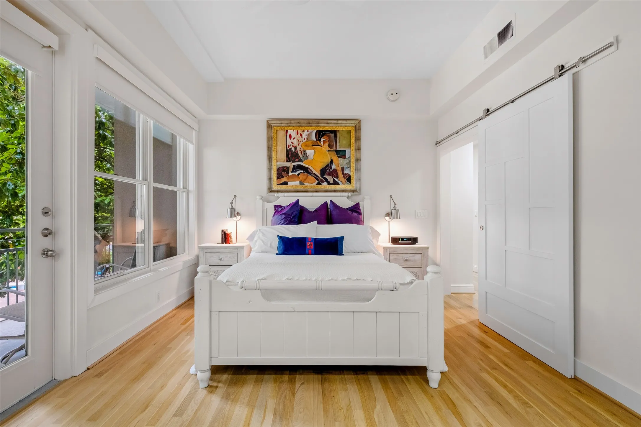 Hardwood flooring, white paneled French doors, white trim, white barn door, and a white paneled headboard