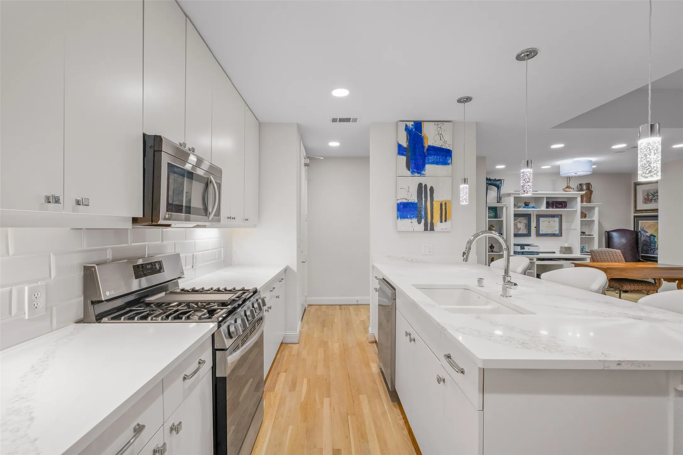 Modern kitchen featuring light wood-finish flooring, white cabinetry with silver hardware, stainless steel appliances, and a white subway tile backsplash