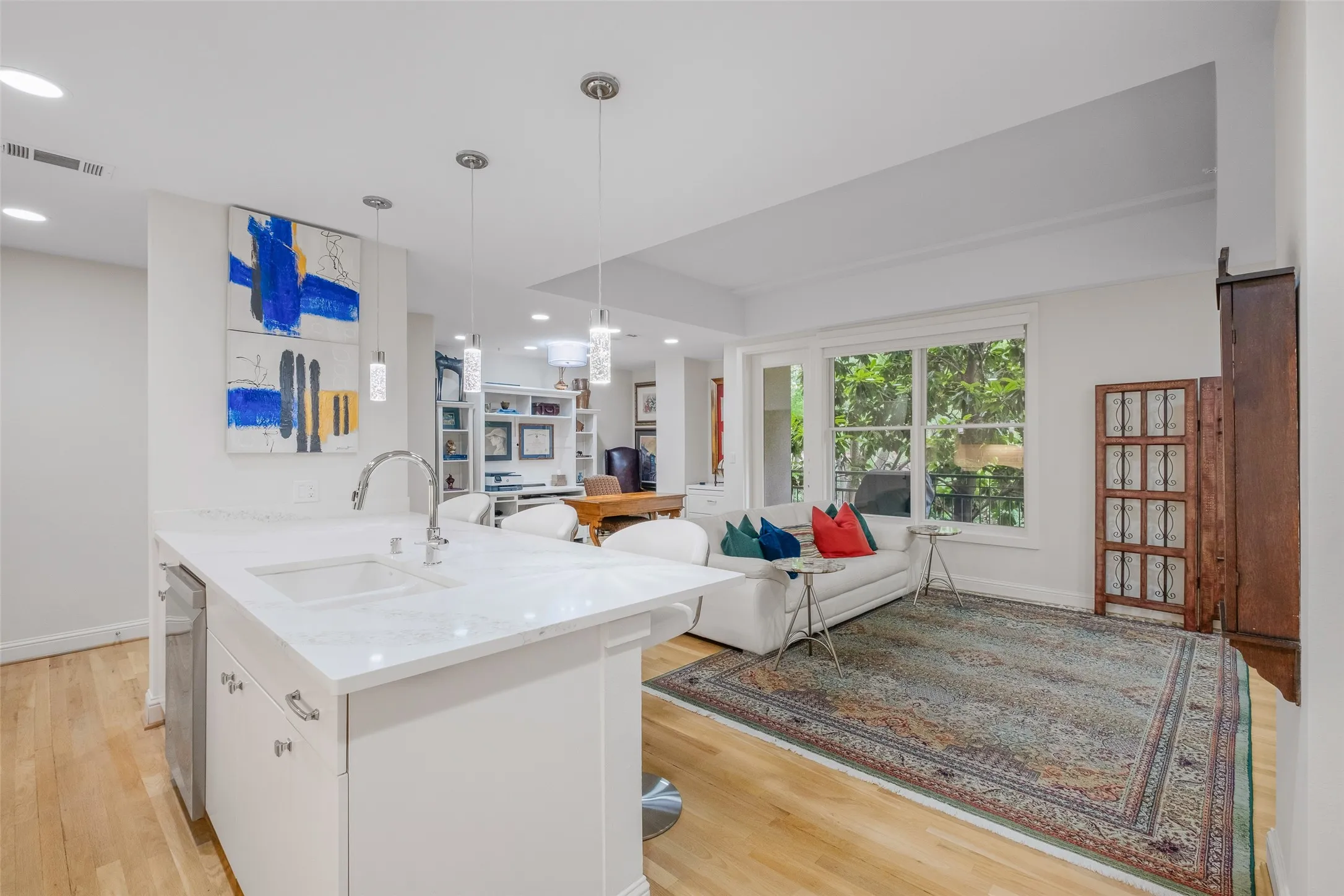 Kitchen island with integrated sink, pendant lighting, wood-finish flooring, built-in shelving, and large windows