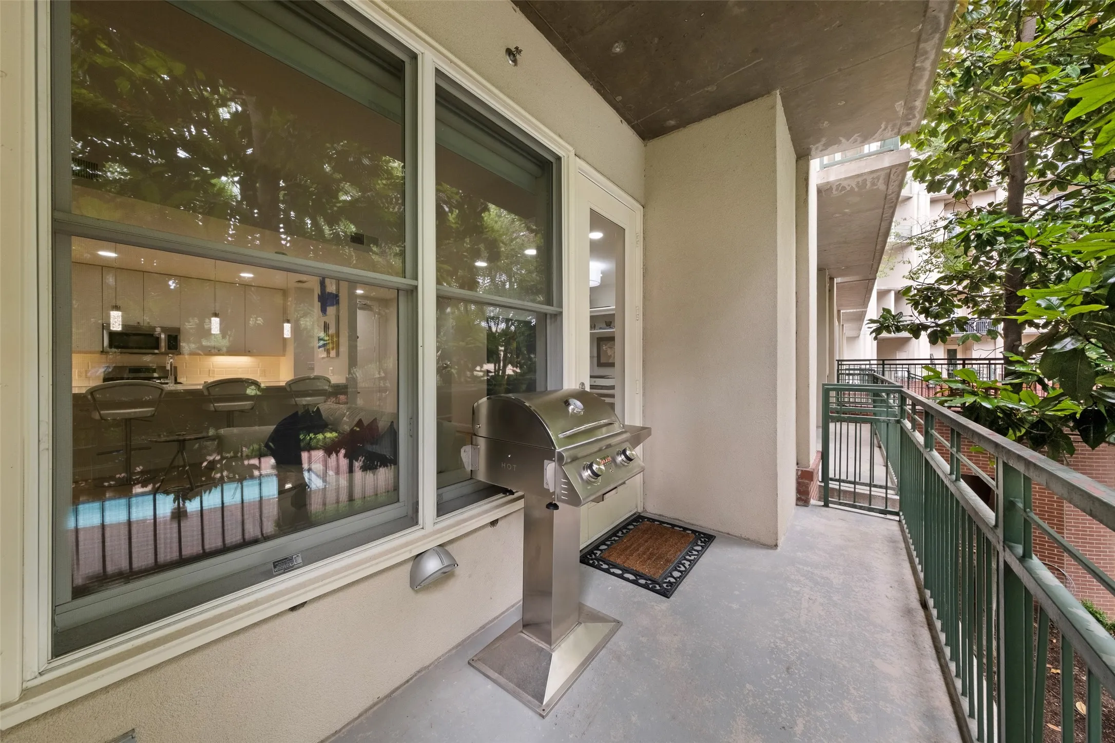 Outdoor balcony with concrete flooring, green metal railing, and direct access to an interior space