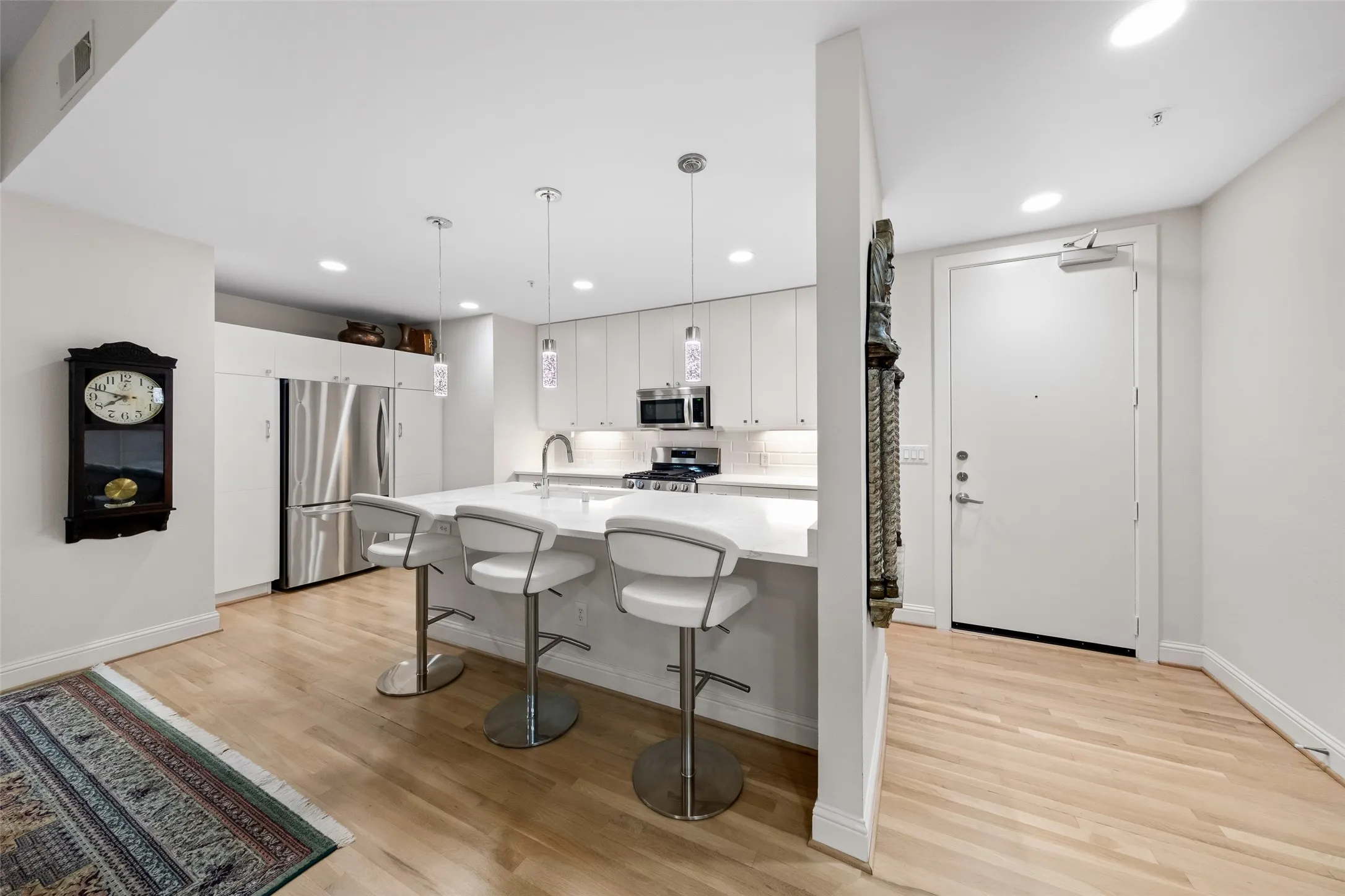 Modern kitchen featuring white cabinetry, stainless steel refrigerator, built-in microwave, a central island with counter seating, and wood-finish flooring throughout