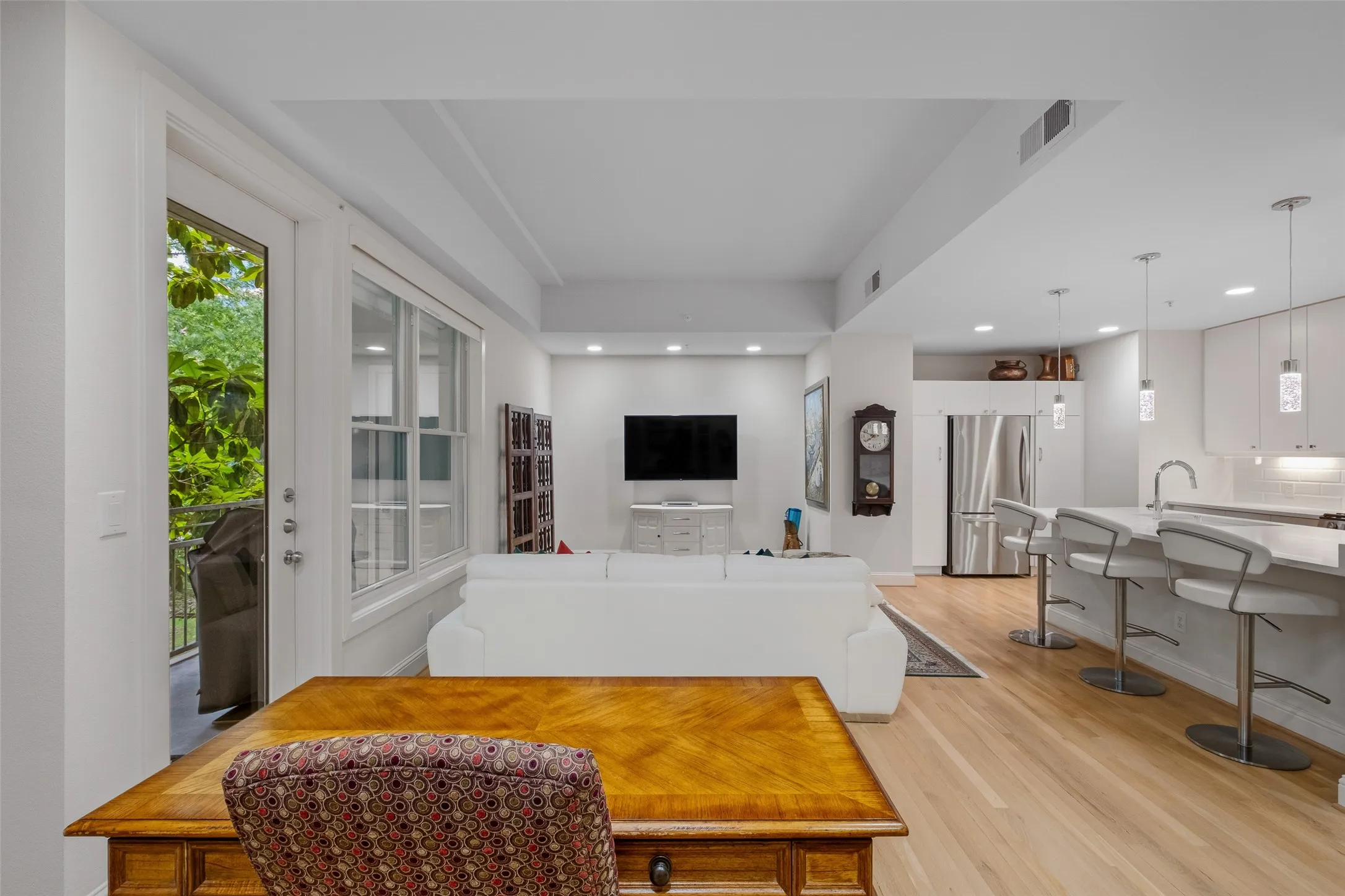 Open-concept living space featuring wood-finish flooring, recessed lighting, and a kitchen with stainless steel appliances, white cabinetry, and a peninsula with seating