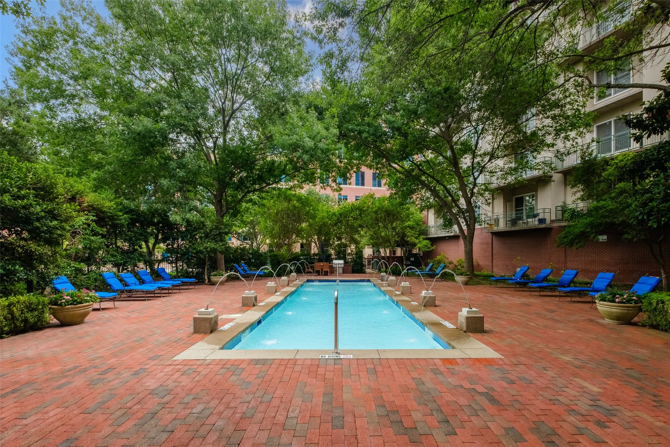 Rectangular swimming pool with multiple water features, surrounded by a red brick paver deck
