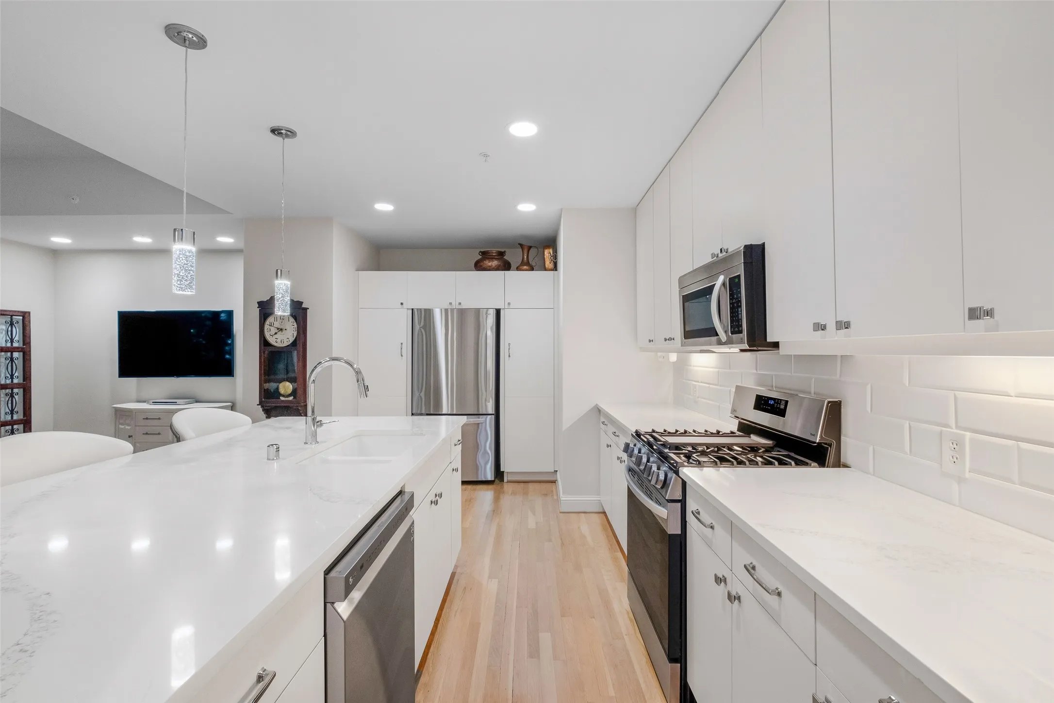 White flat-panel cabinetry, stainless steel appliances, white subway tile backsplash, white countertops, and wood-finish flooring