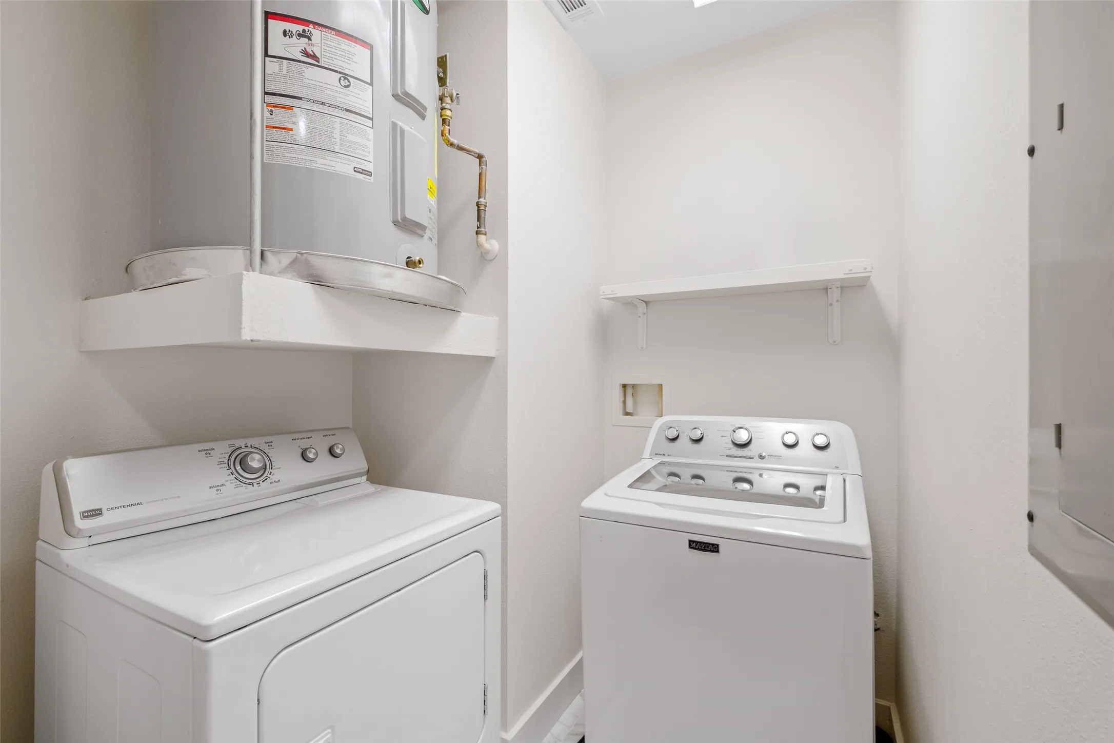 Dedicated laundry area featuring a shelf, water heater, and an additional wall-mounted shelf