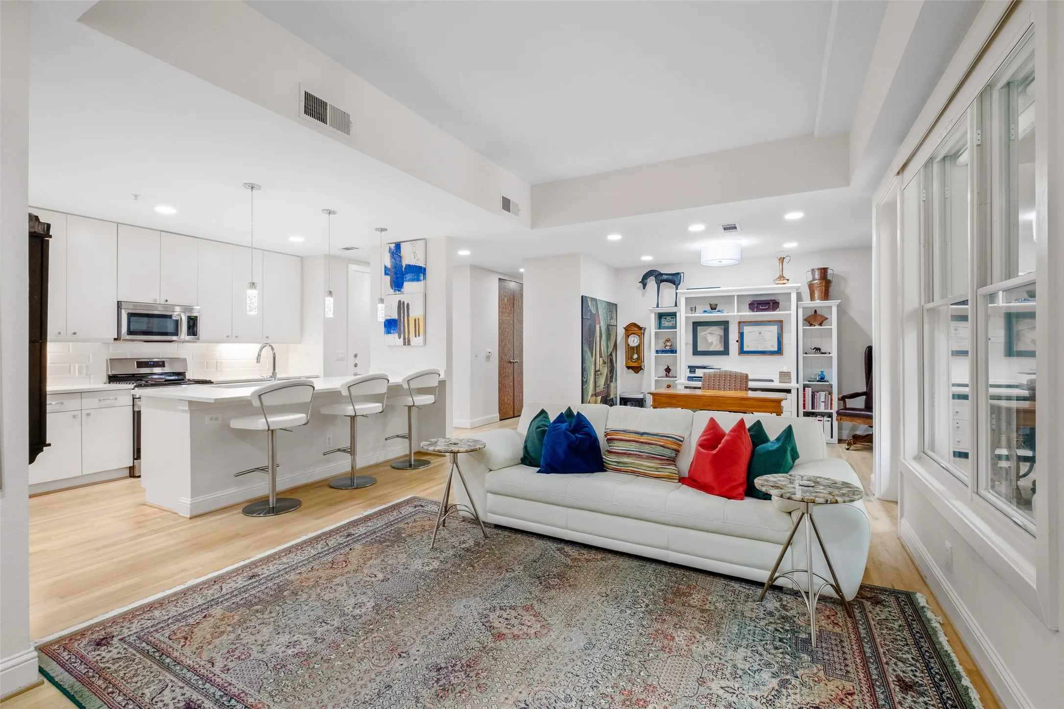 Open-concept living area featuring light wood-finish flooring, white built-in shelving, and white kitchen cabinetry with stainless steel appliances
