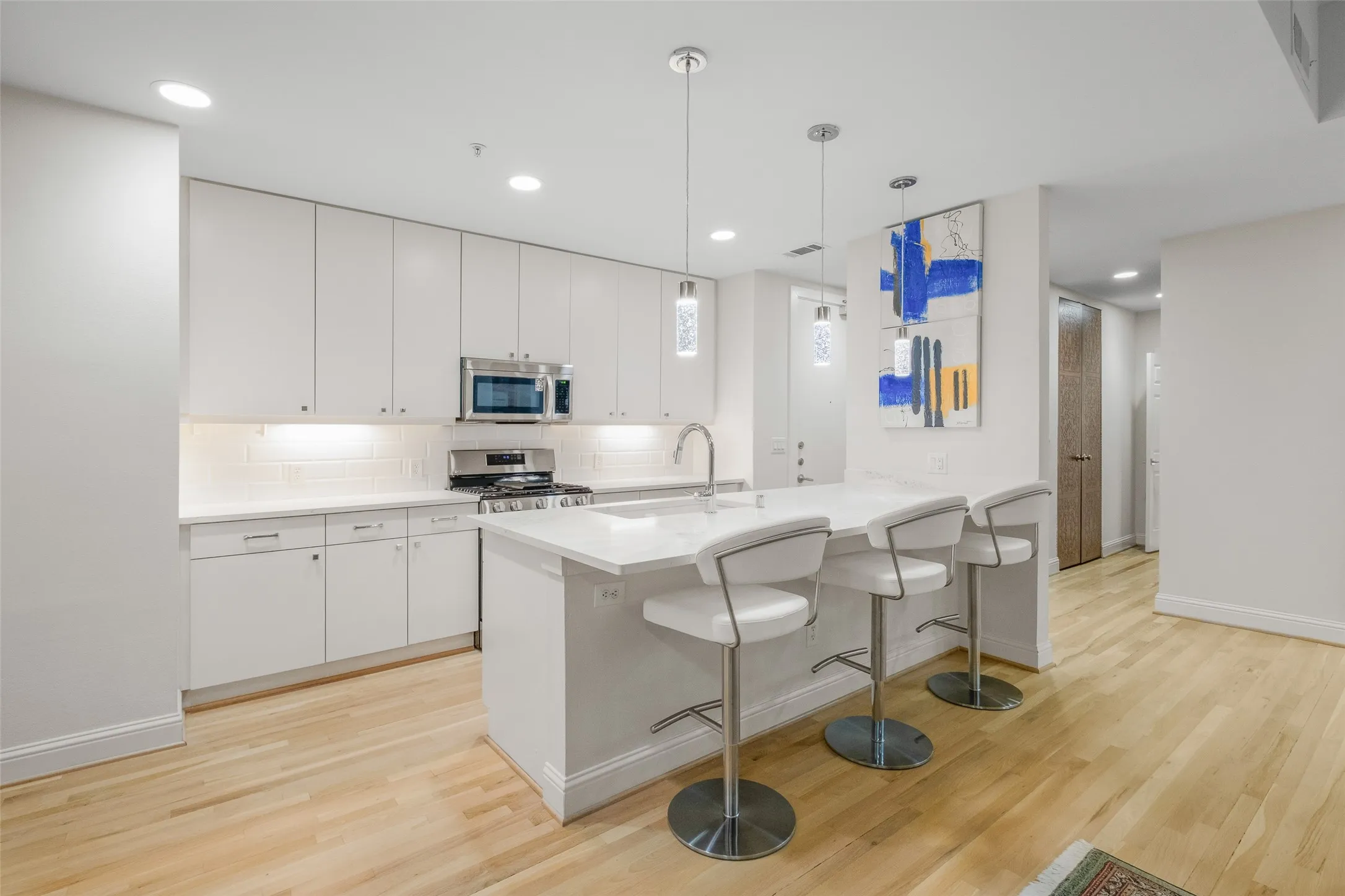Modern kitchen featuring white cabinetry, light countertops, wood-finish flooring, stainless steel appliances, and recessed lighting