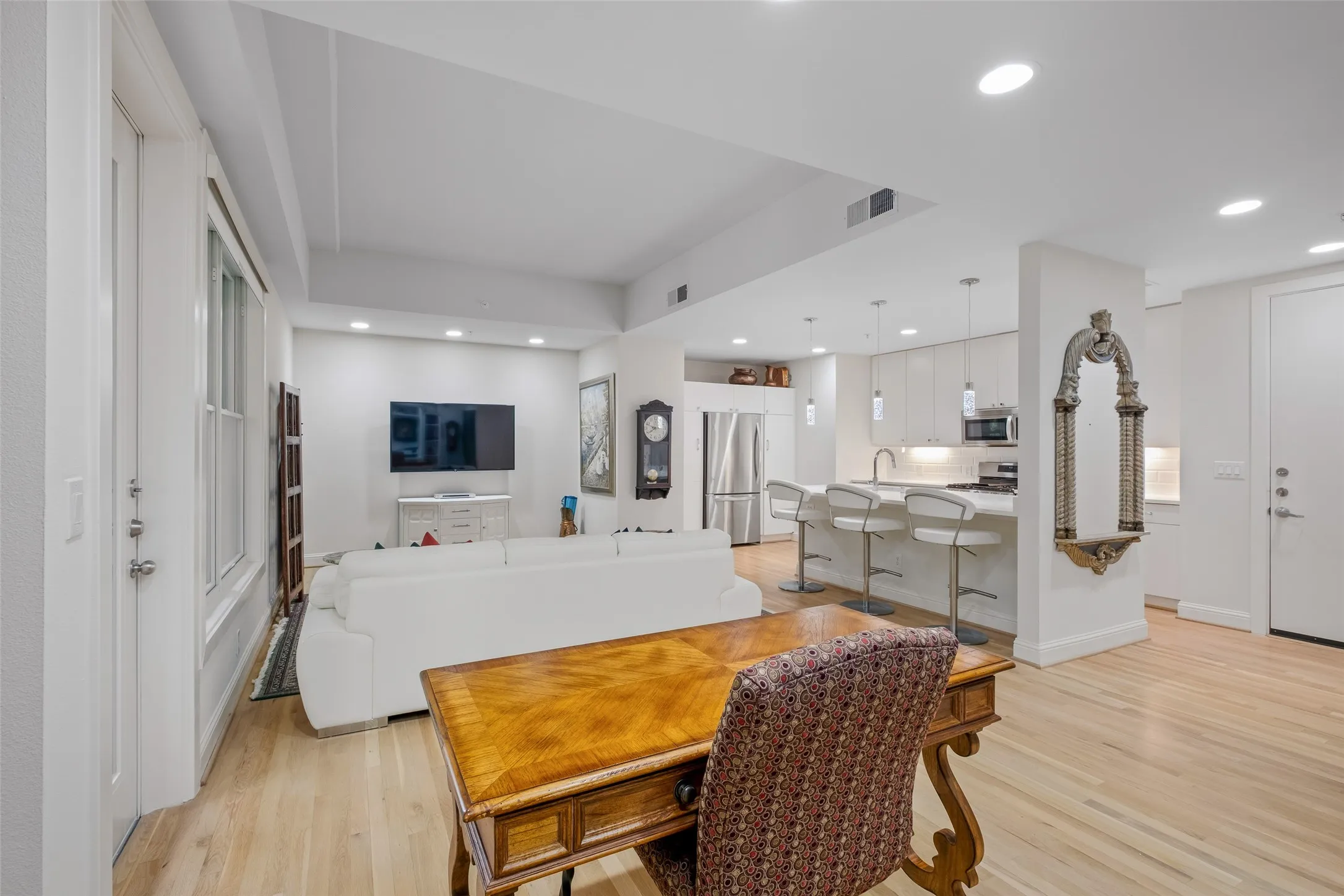 Open-concept living area featuring light wood-finish flooring, recessed lighting, and a kitchen with white cabinetry