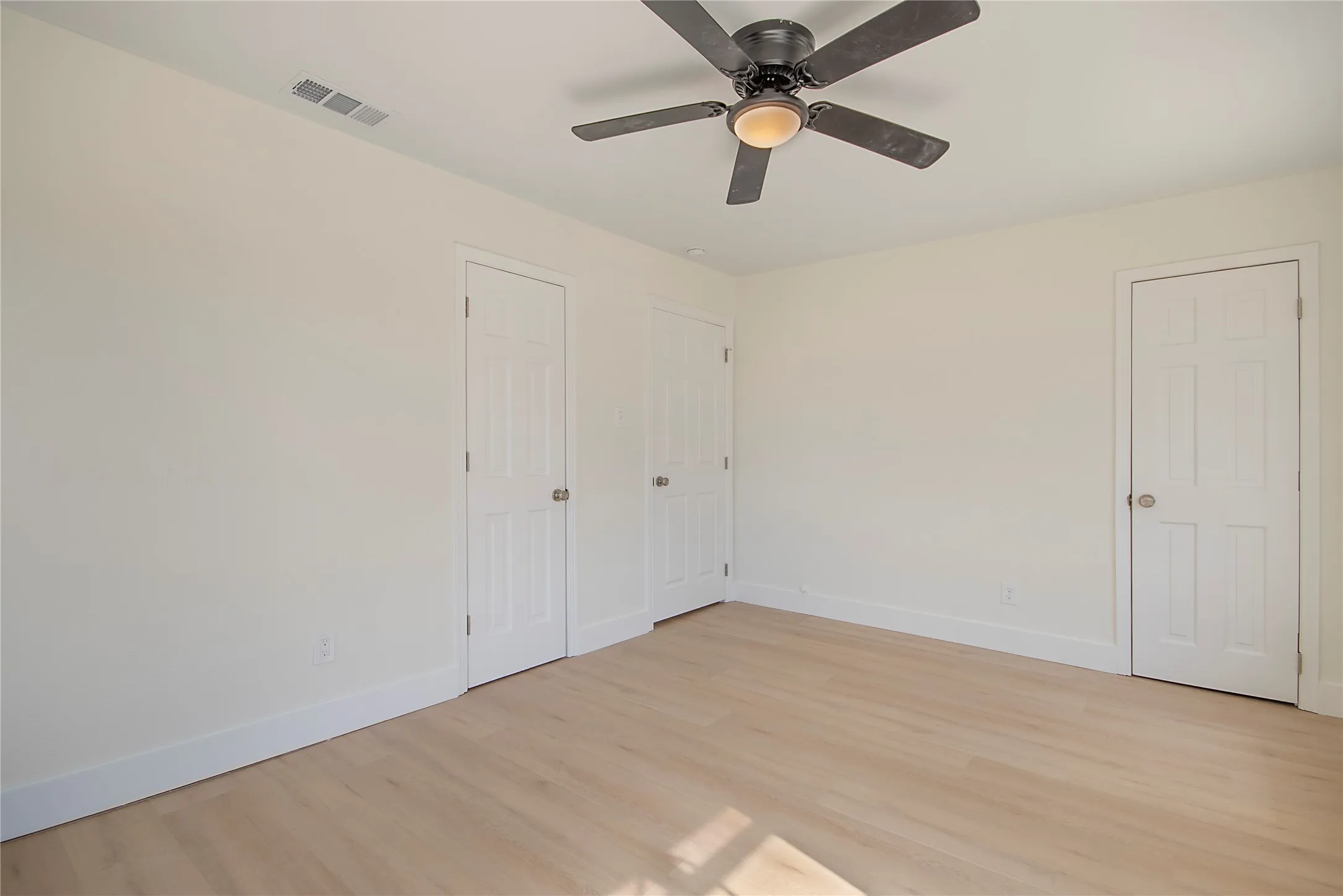 Light-toned wood-finish flooring, white trim, and a ceiling fan with integrated lighting