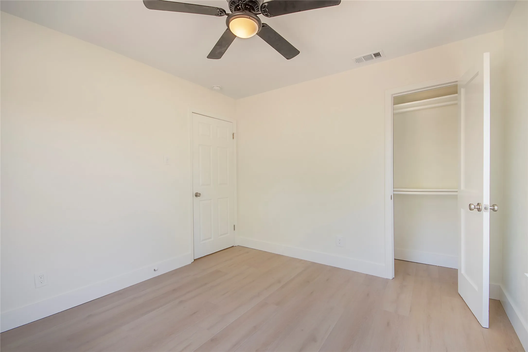 Light wood-finish flooring, built-in ceiling fan with integrated lighting, recessed closet with shelving, and white interior doors